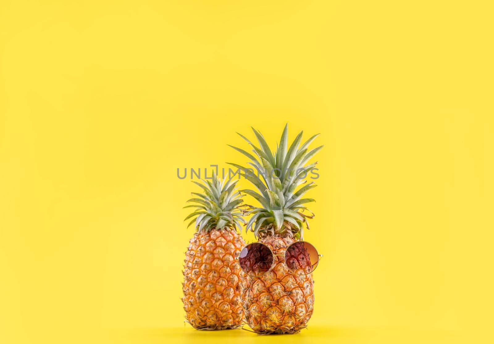 Creative pineapples with sunglasses isolated on yellow background, summer vacation beach idea design pattern, copy space, close up, blank for text by ROMIXIMAGE