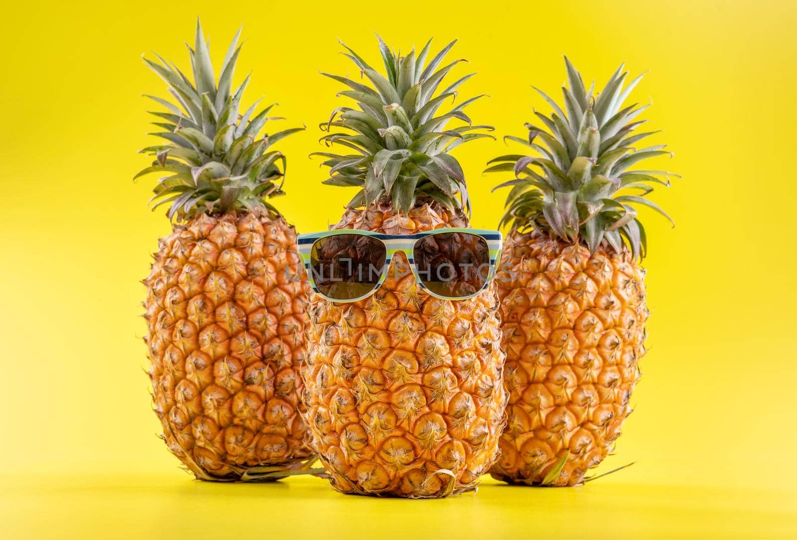 Creative pineapple looking up with sunglasses and shell isolated on yellow background, summer vacation beach idea design pattern, copy space close up by ROMIXIMAGE