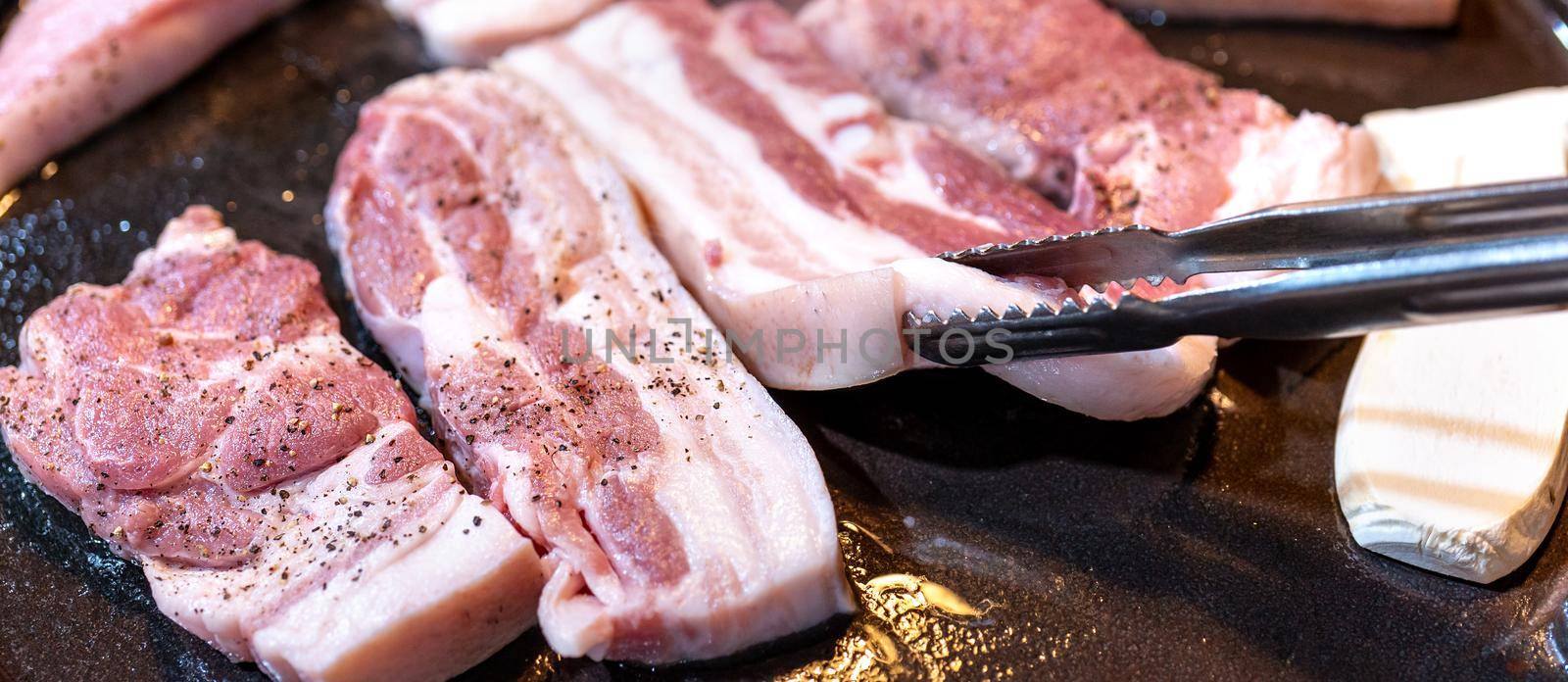 Pan-fried black pork meal in Korea restaurant, fresh delicious korean food cuisine on iron plate with lettuce, close up, copy space, lifestyle by ROMIXIMAGE
