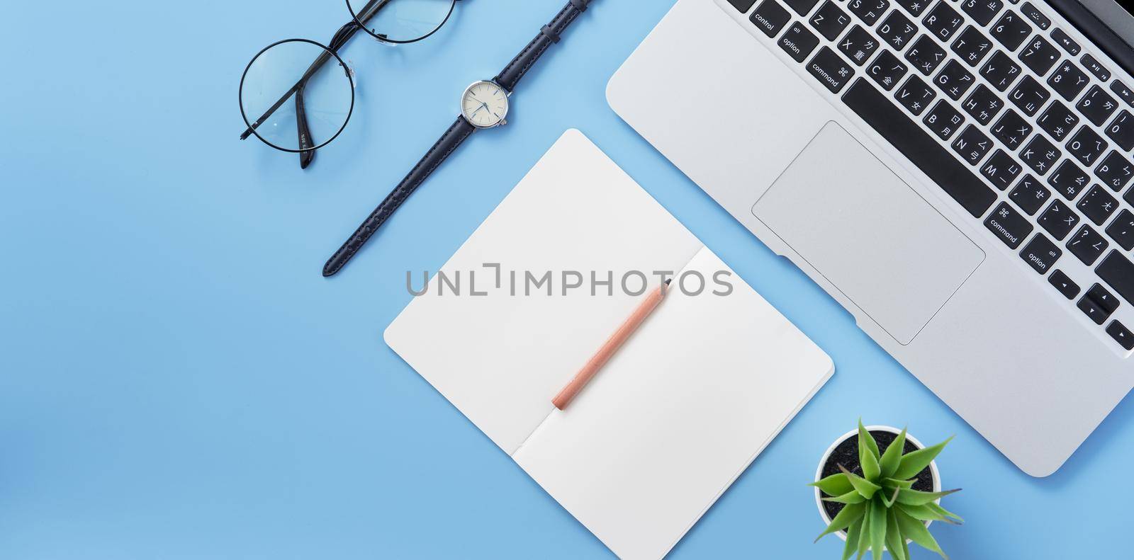 Girl write on open white book or accounting on a minimal clean light blue desk with laptop and accessories, copy space, flat lay, top view, mock up