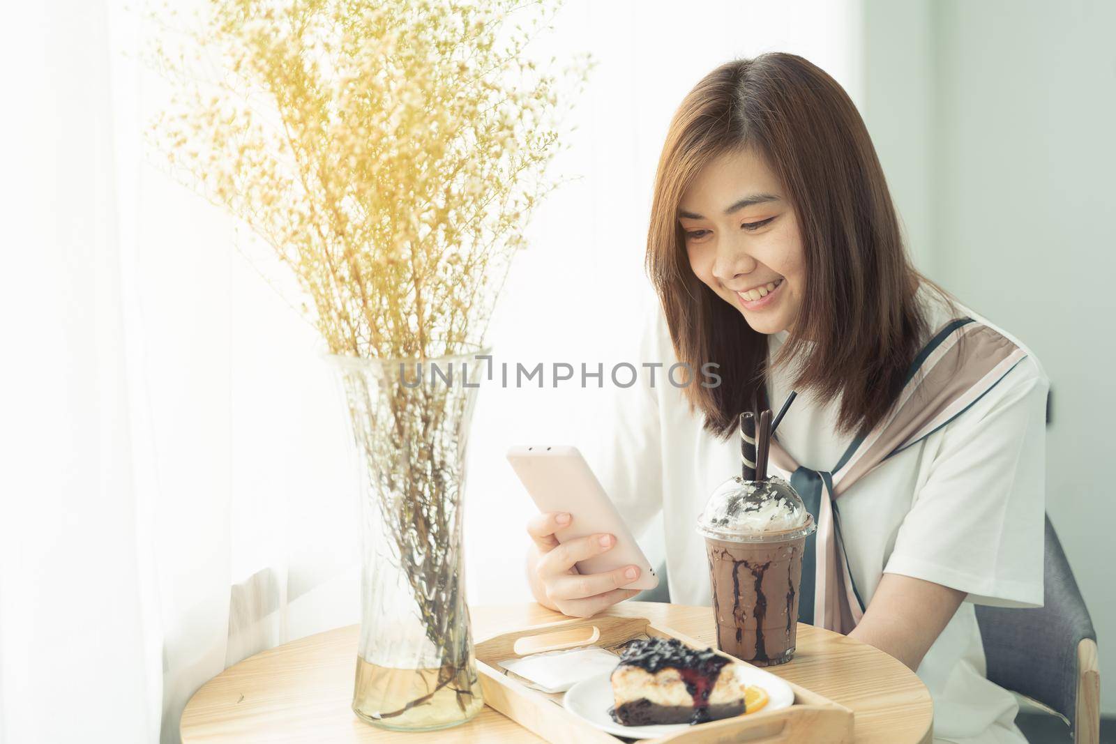 beautiful girl smiling using mobile phone in the cafe, girl eat coffee and cake by Wmpix
