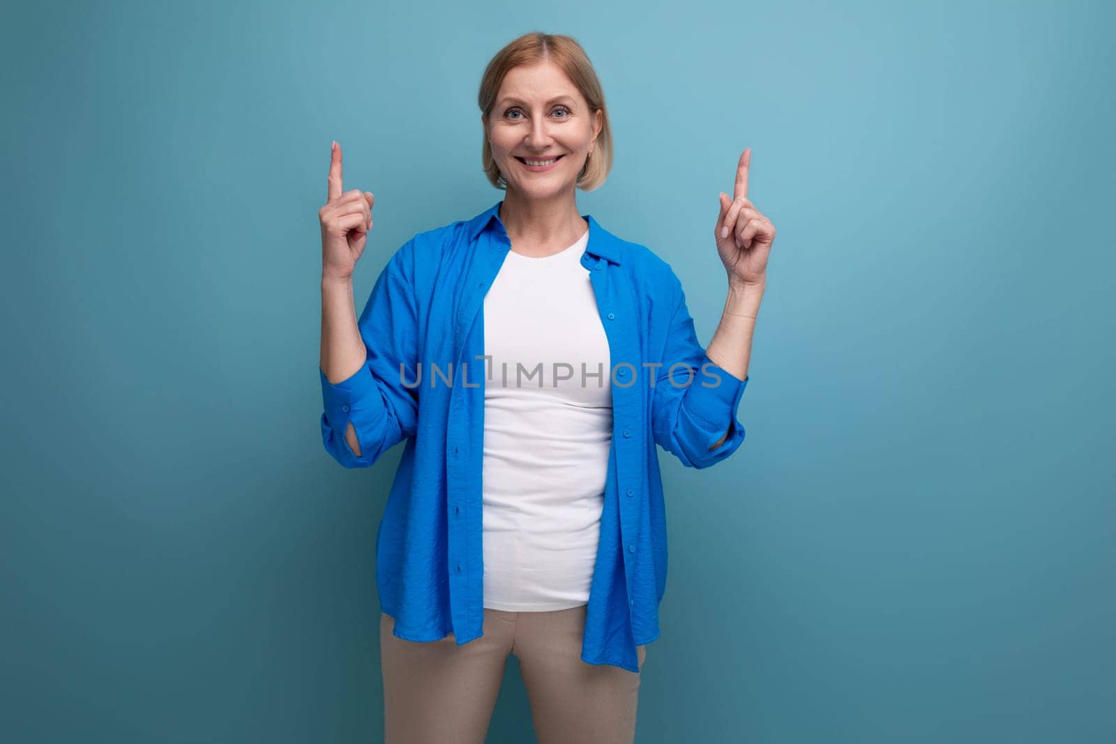 confident blonde 50s woman on blue background with copyspace.