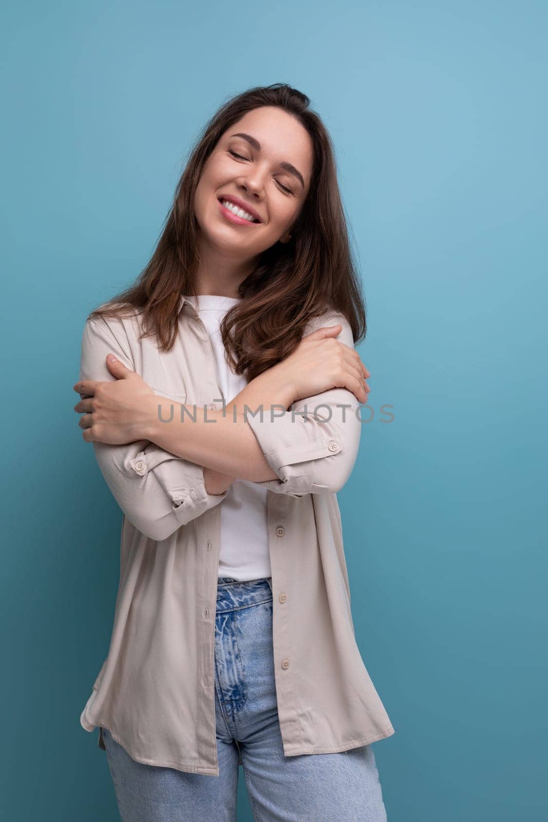 romantic dreaming european young brunette woman in shirt and jeans on blue background by TRMK