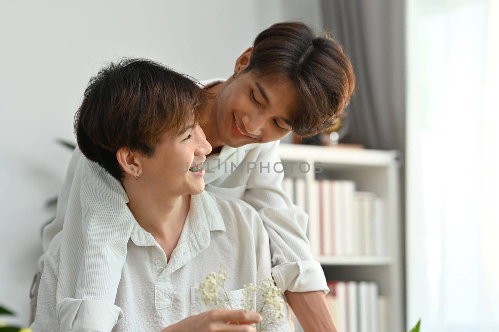 Affectionate romantic male gay couple spending time together, enjoying arranging flowers in cozy home. LGBT, homosexual and love by prathanchorruangsak
