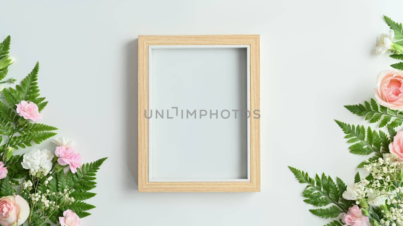Blank wooden picture frame with pink rose, carnation and fern leaves on white background. Spring floral background, copy space.