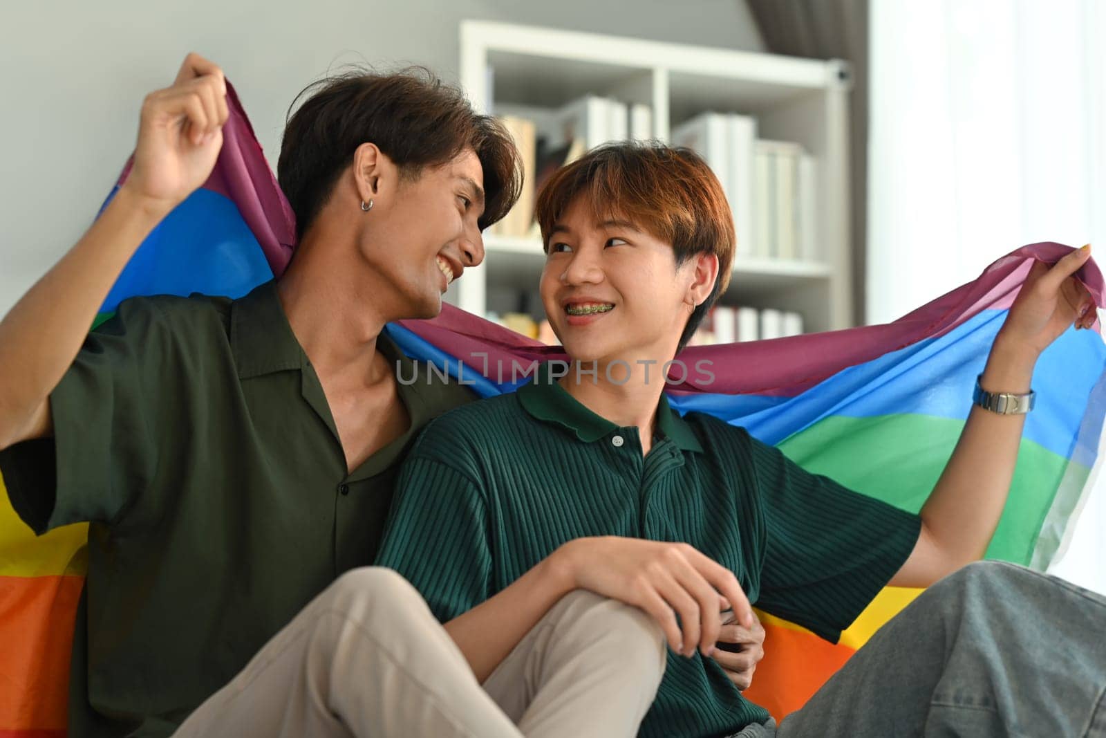 Image of gay couple embracing under LGBT pride flag. LGBT, love and human rights concept.