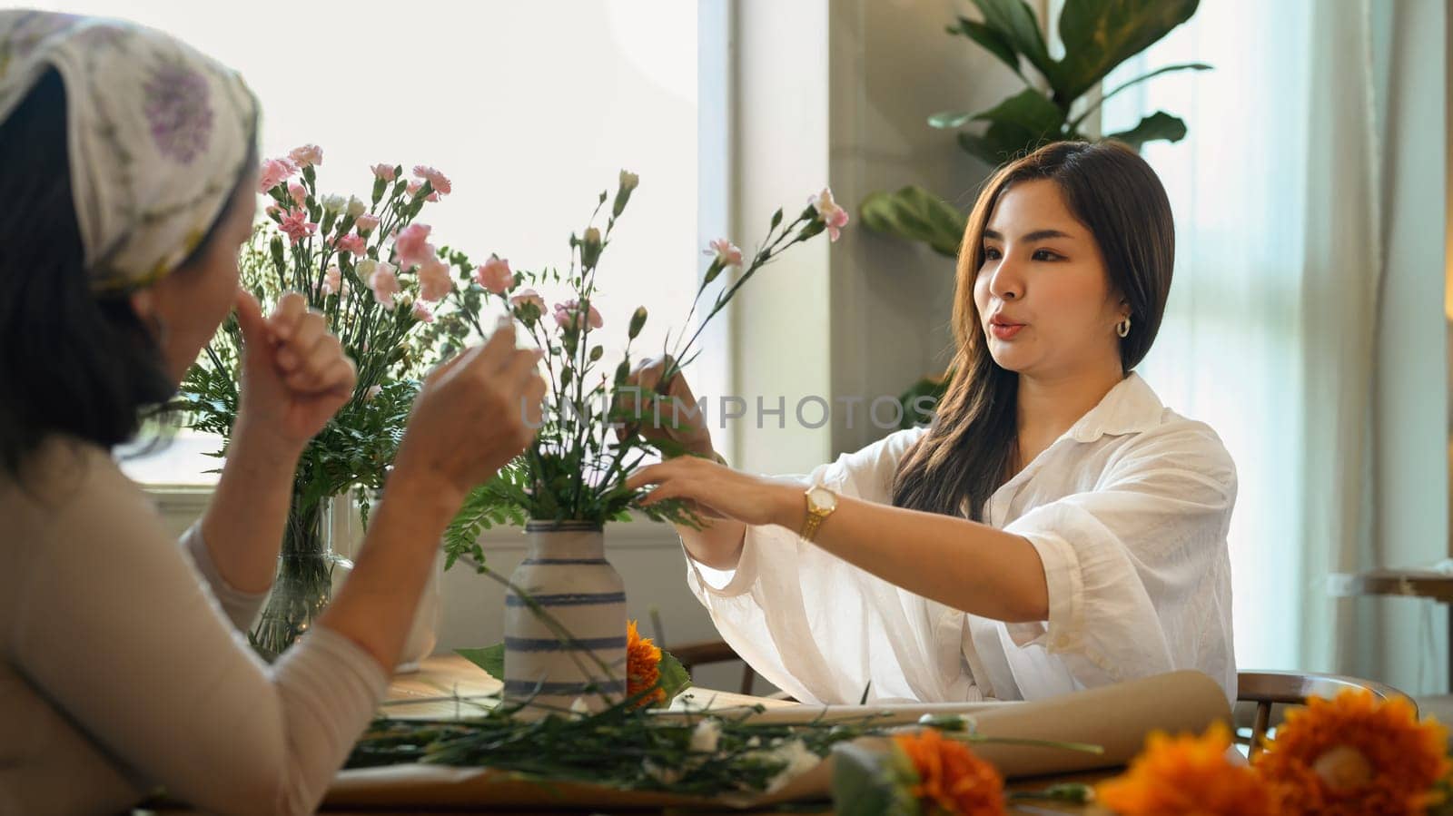 Pretty young asian woman and her senior mother making a bouquet with fresh flowers at floral shop. Small business concept.