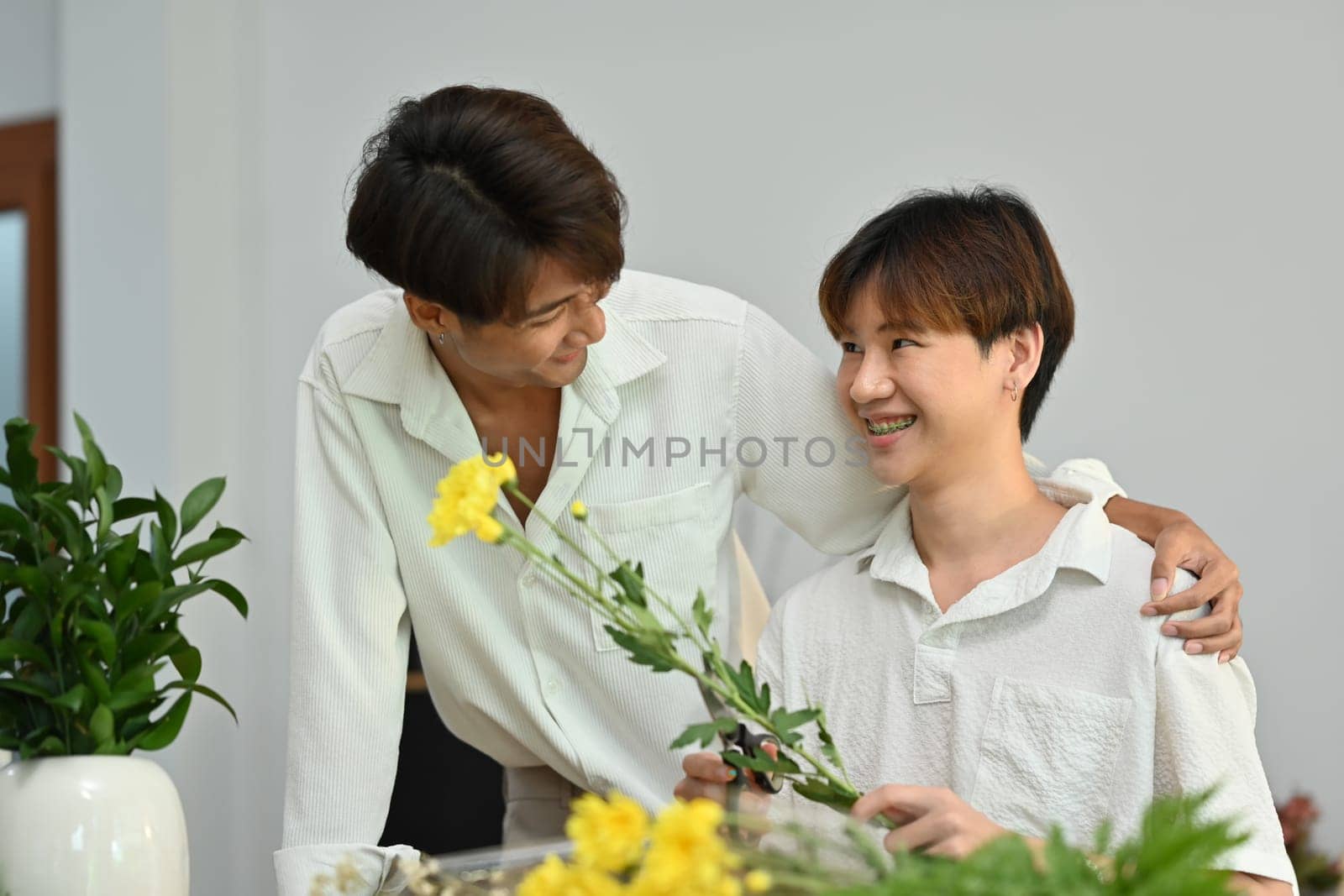 Affectionate romantic male gay couple spending time together, enjoying arranging flowers in cozy home. LGBT, homosexual and love.