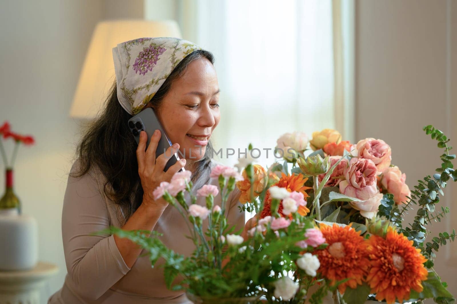 Smiling senior woman flower shop owner taking orders from client on mobile phone. Floristry and small business concept.