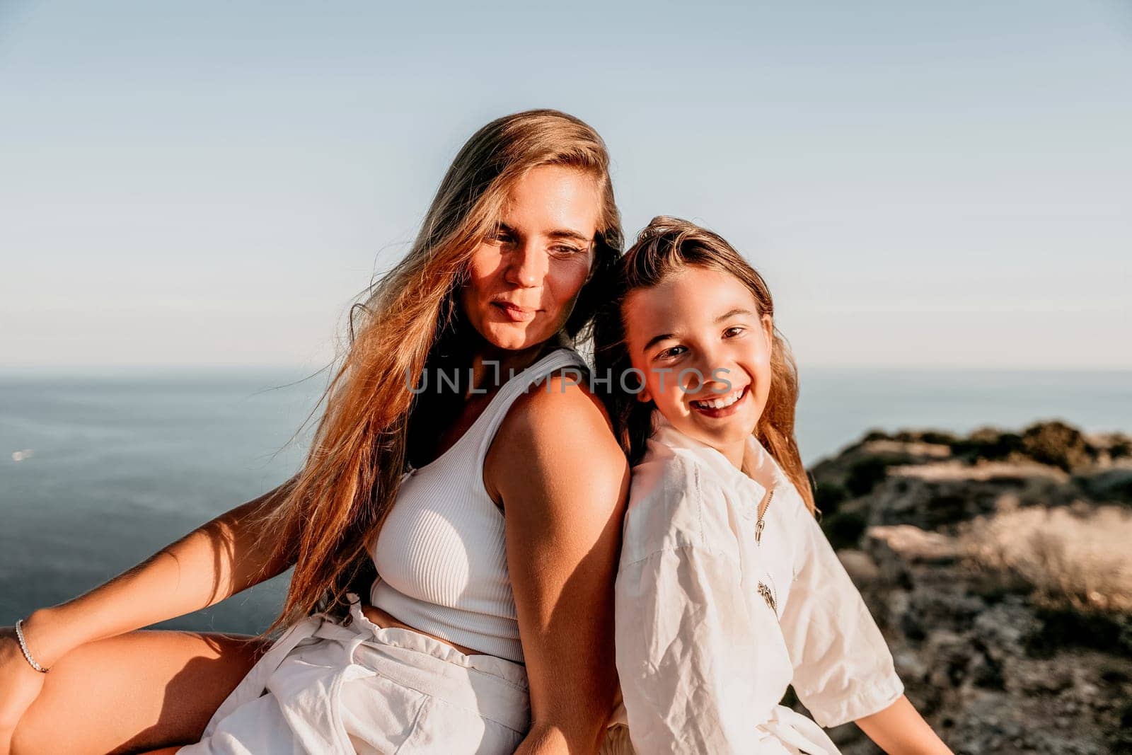 Sea family vacation together, happy mom and teenage daughter hugging and smiling together over sunset sea view. Beautiful woman with long hair relaxing with her child. Concept of happy friendly family. by panophotograph