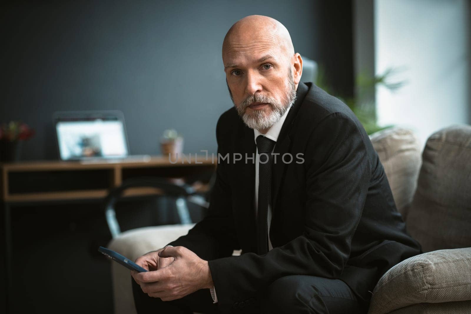 Sad man in a black suit who is looking for job. The mature businessman, with his distinguished silver beard, can be seen browsing the internet in search of work. High quality photo