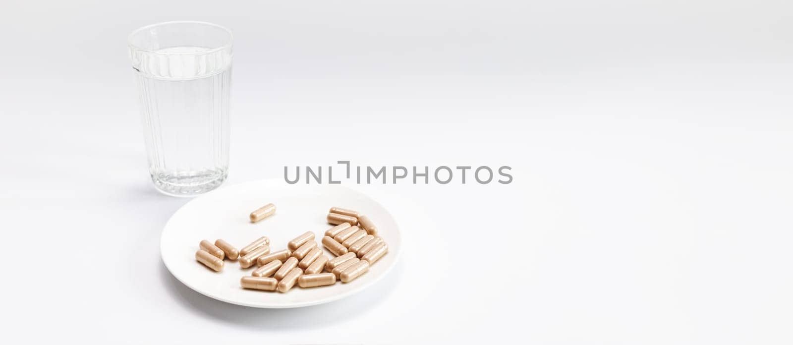 Banner Group Of Slippery Elm Capsules on plate, Glass Of Water On White Background. Traditional, dietary supplement. Holistic remedy, medication Horizontal Plane, Copy Space For Text by netatsi