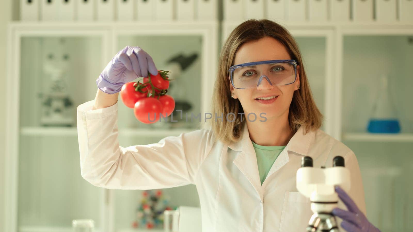 Scientist chemist in protective glasses holding branch of tomatoes in hands in chemical laboratory. Genetically modified food production concept