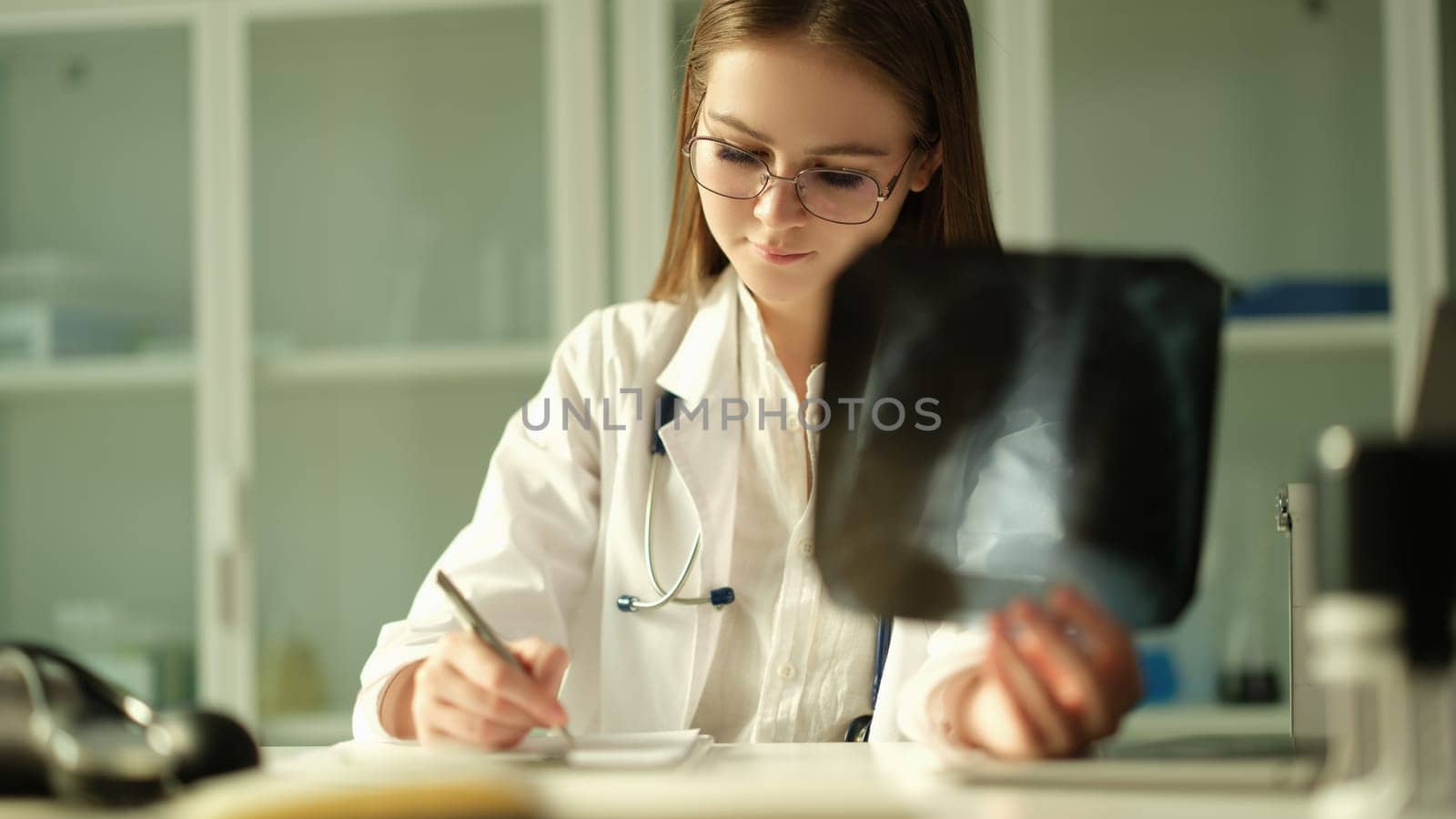 Doctor pulmonologist examining x-ray lungs and writing patient medical history in clinic. Xray diagnosis of pneumonia concept