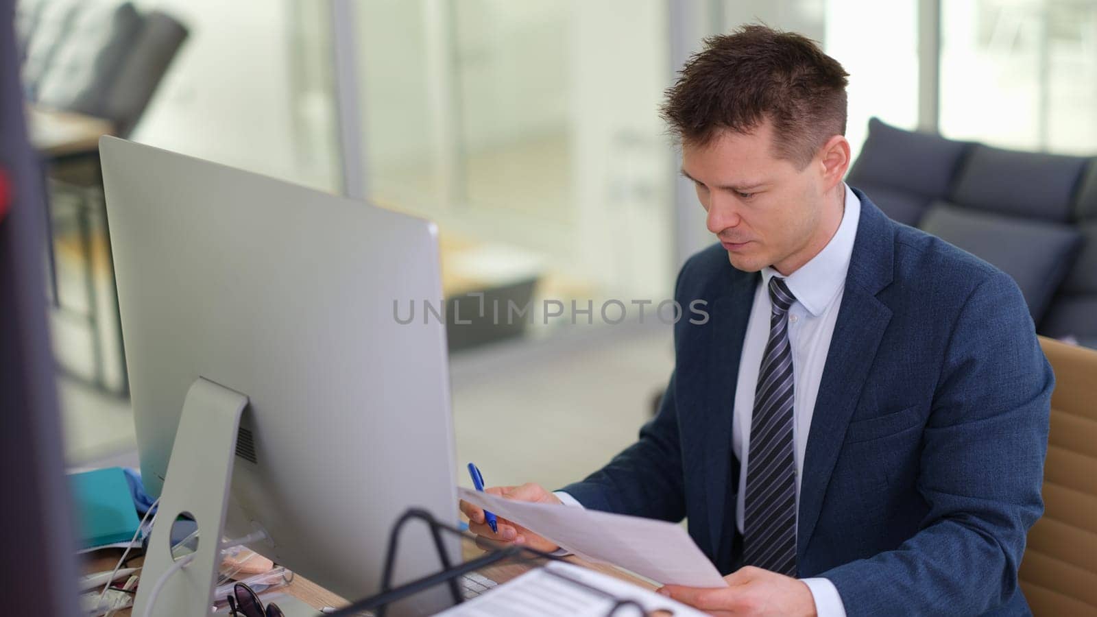 Businessman studying paper document in front of computer in office by kuprevich