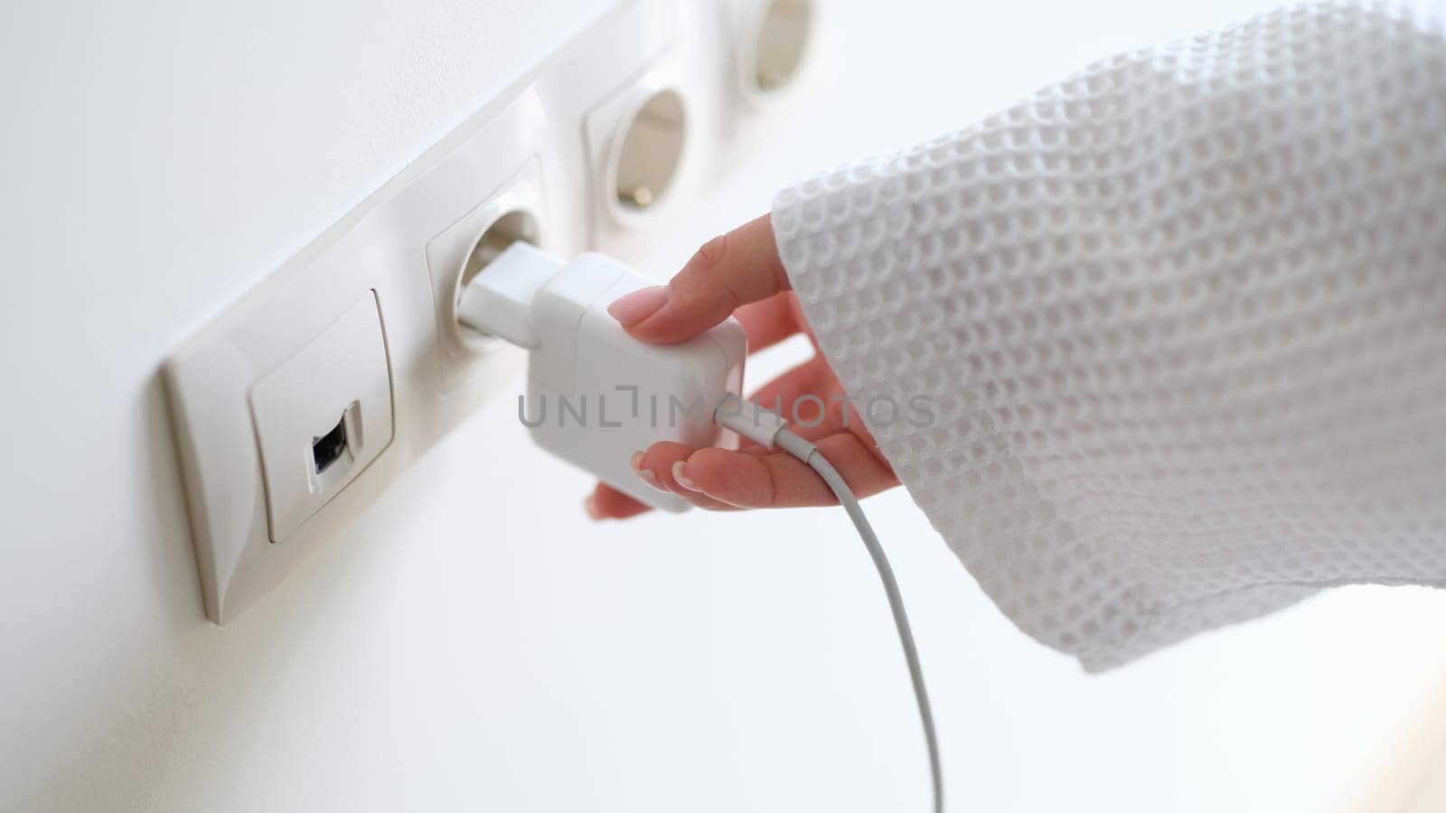 Woman in white bathrobe inserting plug into outlet at home with hand closeup. Energy saving concept