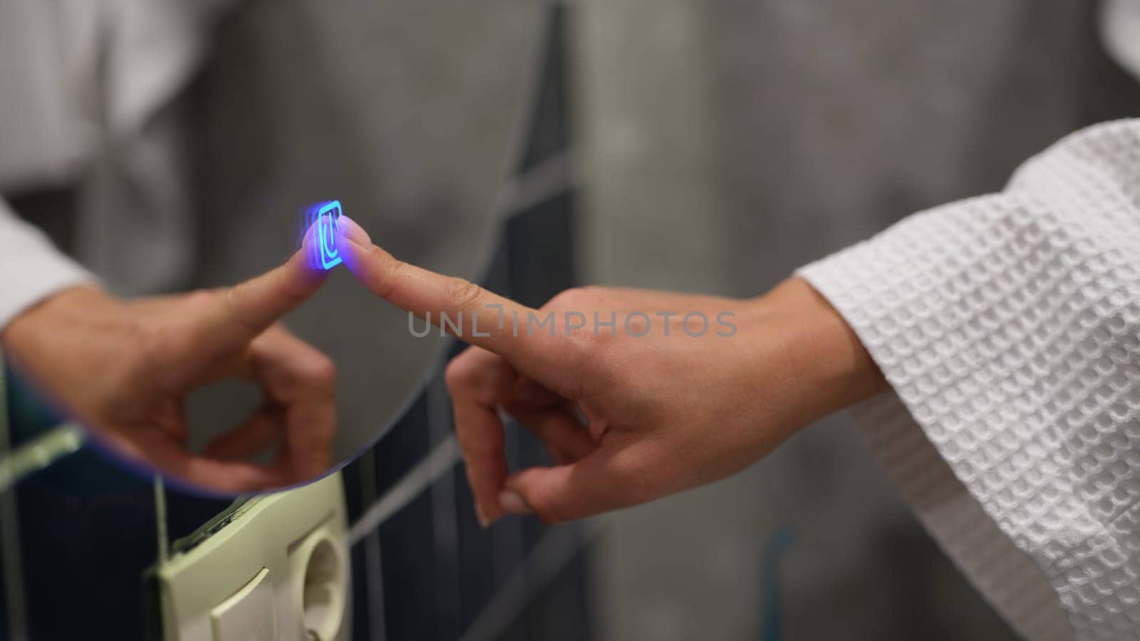 Woman finger pressing blue luminous button on bathroom mirror closeup. Modern electrical concept