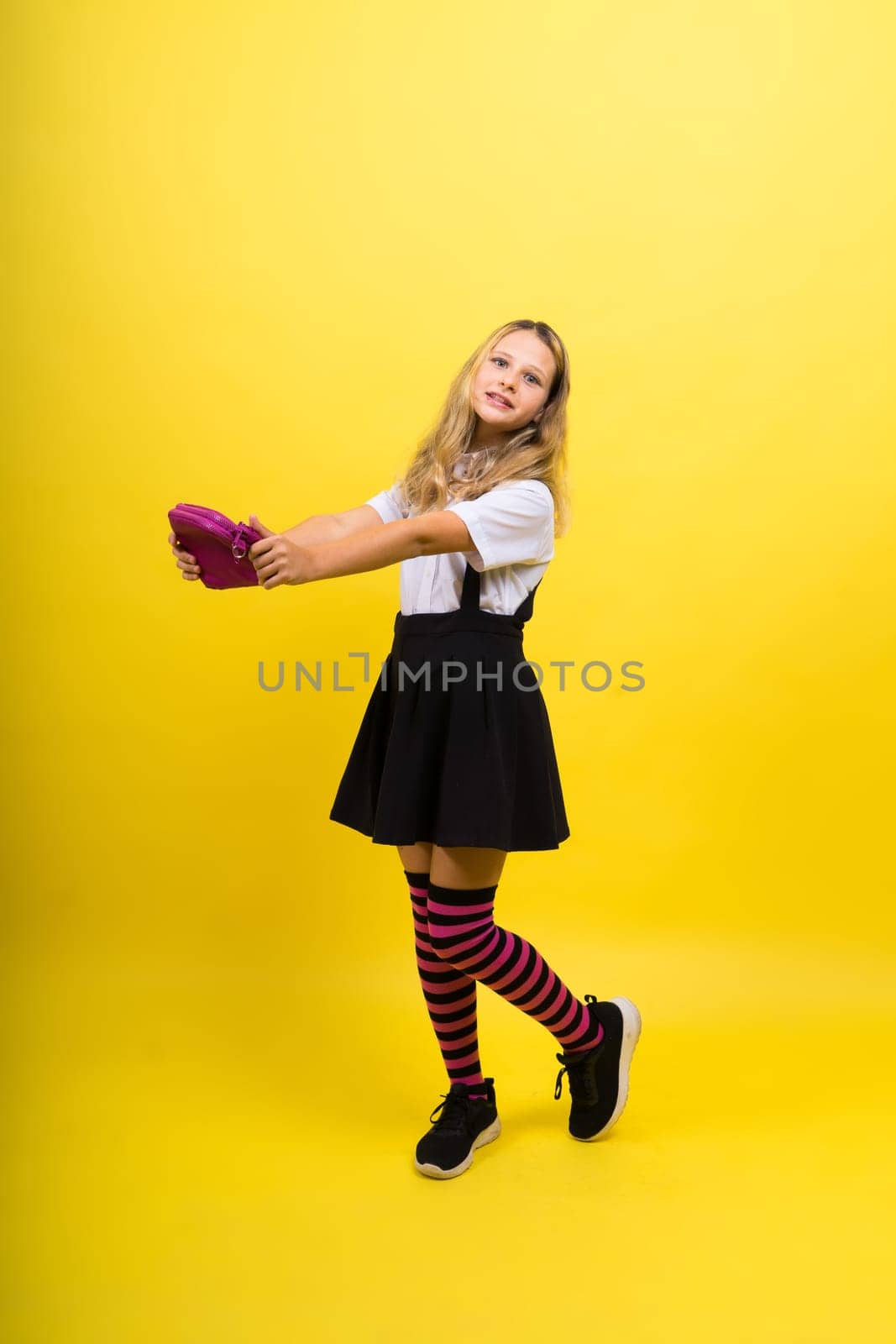 Little teenager girl with pencil case on a yellow background