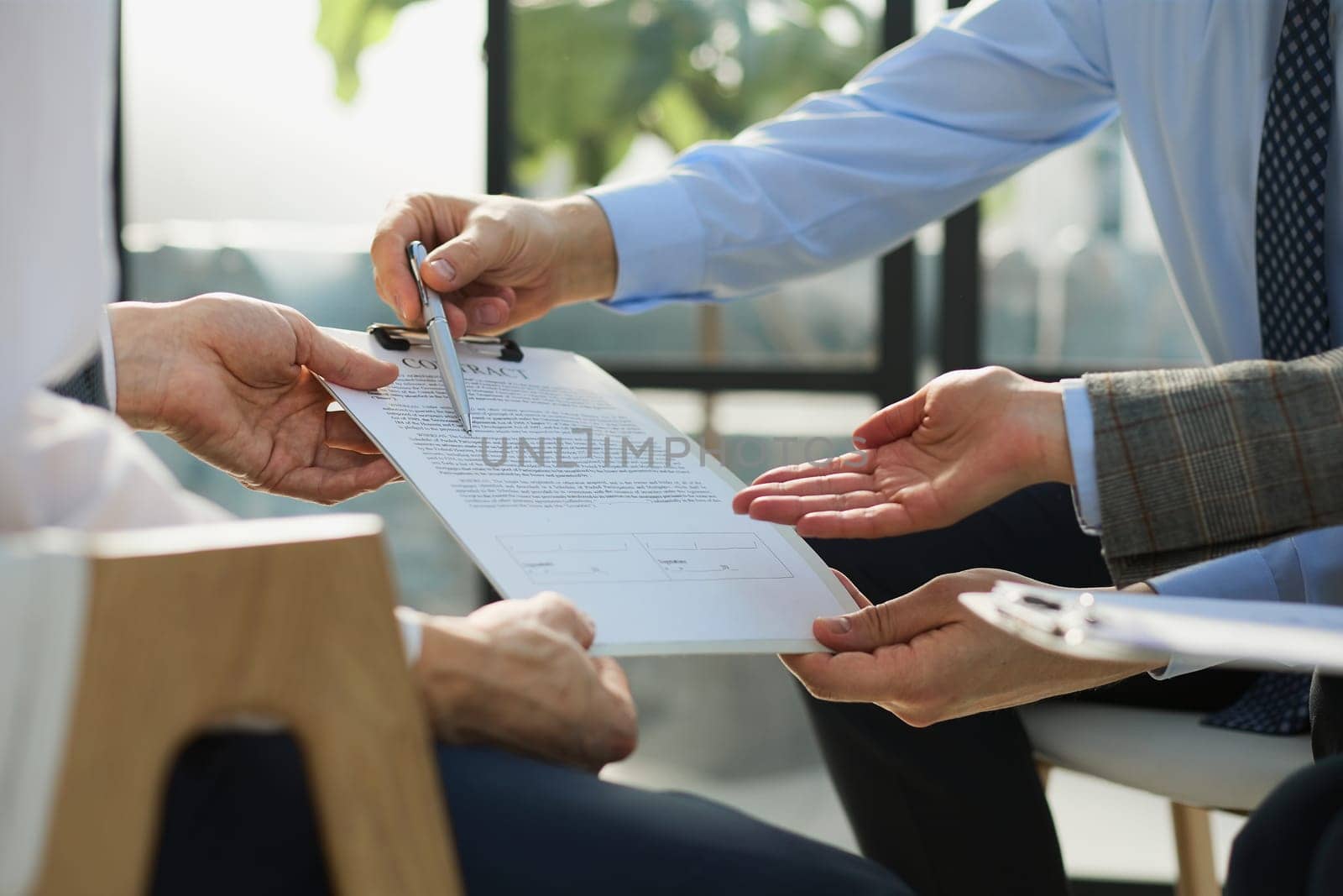Closeup business deal meeting, businessman carefully reviewing terms and condition of contract agreement papers in office.