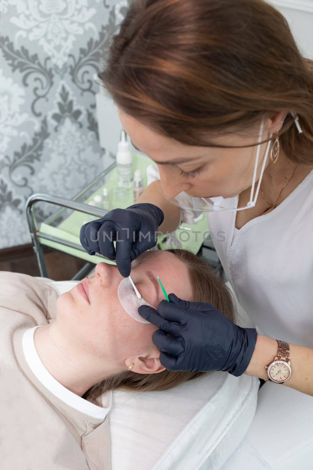 Beautician Cleans Lashes Of Young Woman With Eye Patches Before Laminating Eyelash Beauty Treatment. Curling, Staining, Extension Procedures For Lashes. Vertical Plane. Step By Step. by netatsi
