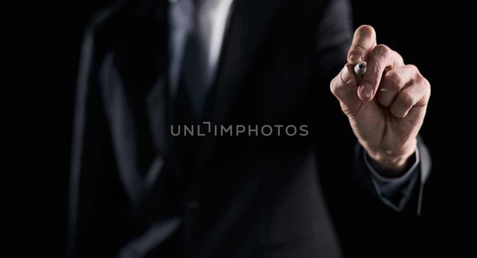 A hand holding a marker turned to the camera against a dark background