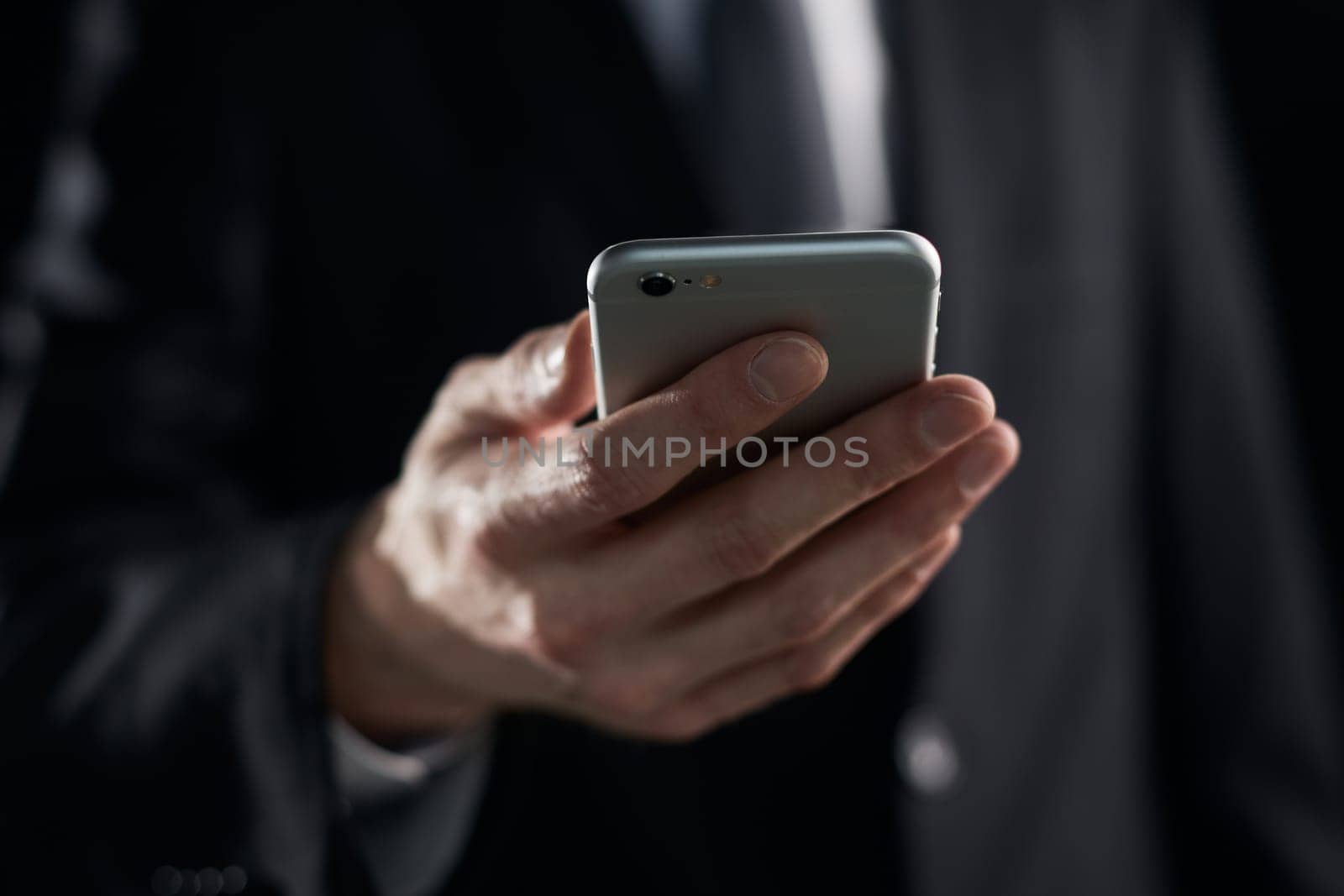 businessman looking at smartphone screen in hand on dark background