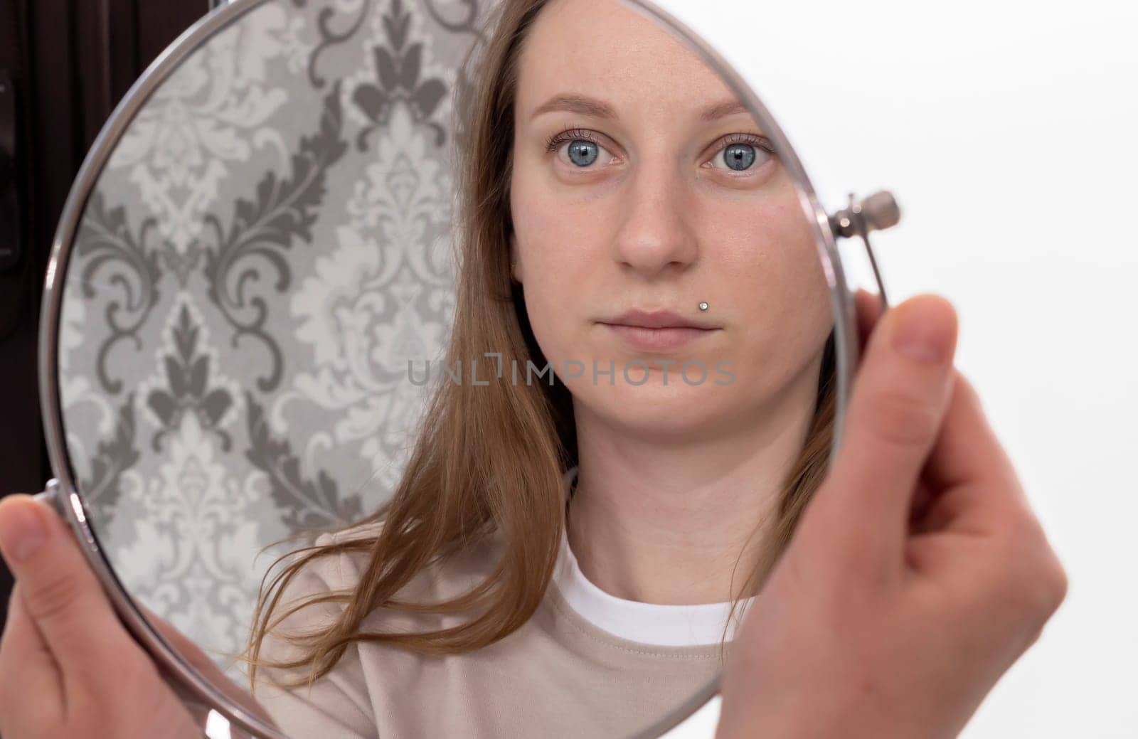 Portrait Of Caucasian Woman After Eyelash Lamination Procedure Looking At Own Reflection In Mirror. Horizontal Plane. High quality photo