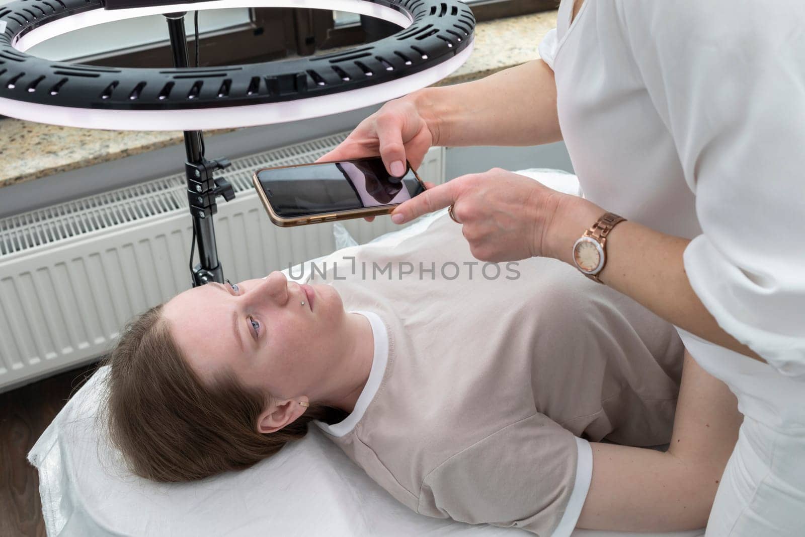 Beautician Takes Photo Of Caucasian Woman After Eyelash Lamination Procedure, Result On Smartphone, Gadget in Beauty Salon. Horizontal Plane. High quality photo
