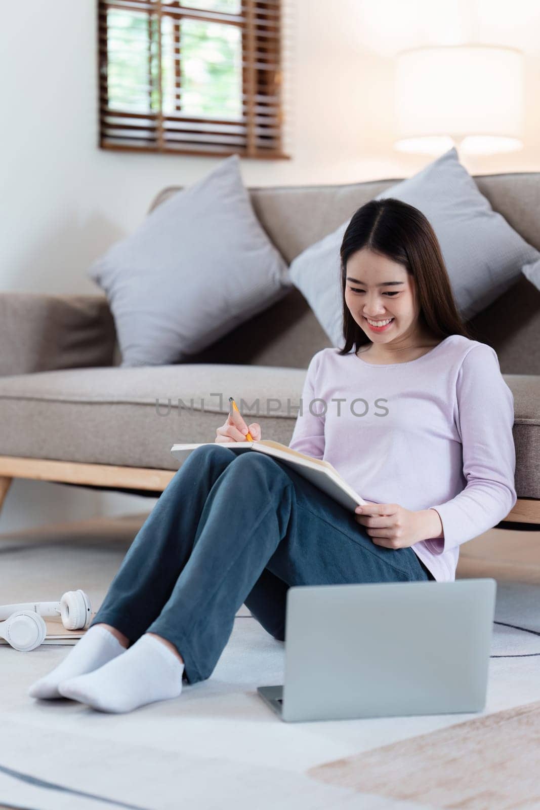 Online education, e-learning. Asian woman in stylish casual clothes, studying using a laptop, listening to online lecture, taking notes, online study at home by itchaznong