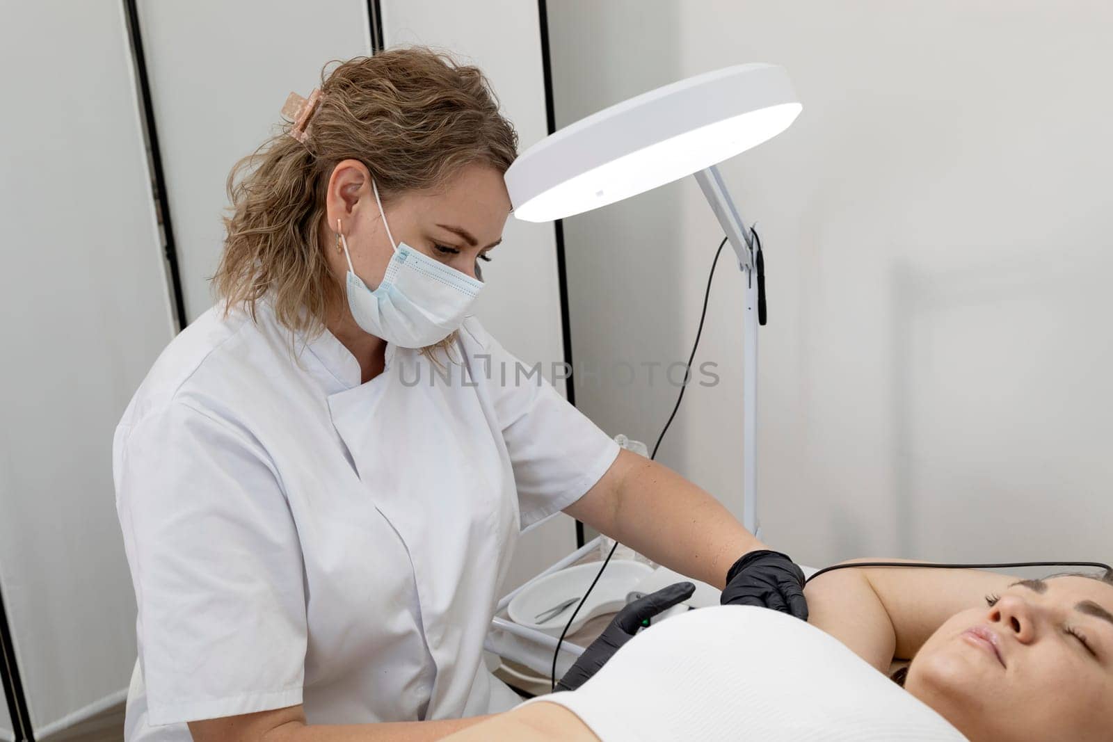 Electrologist Doing Underarm Hair Removal Procedure With Electrolysis To White Young Woman, Electric Epilation In Beauty Salon. Horizontal Plane. Authentic High quality photo