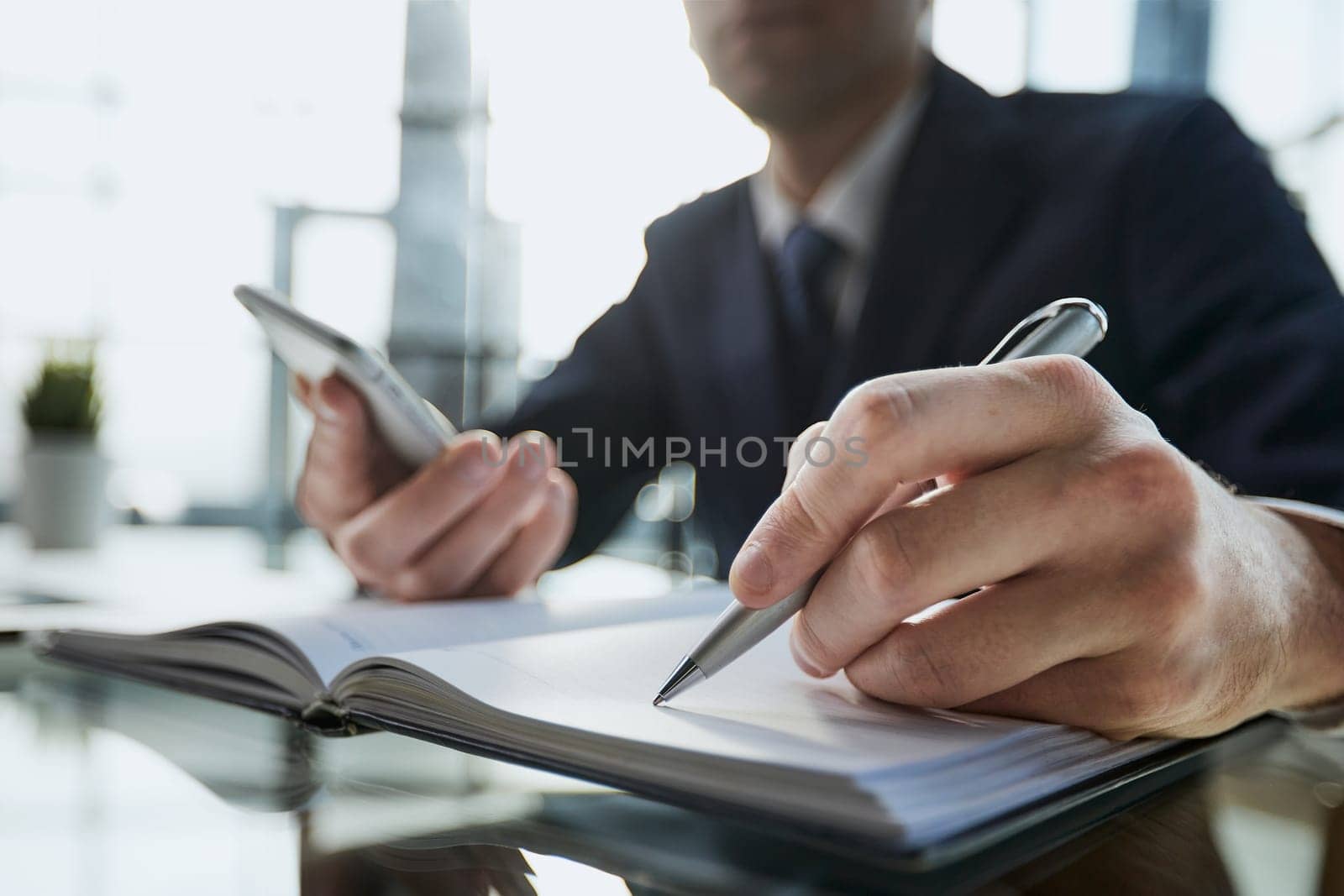 Close up of woman's hands writing in spiral notepad placed on wooden desktop with various items