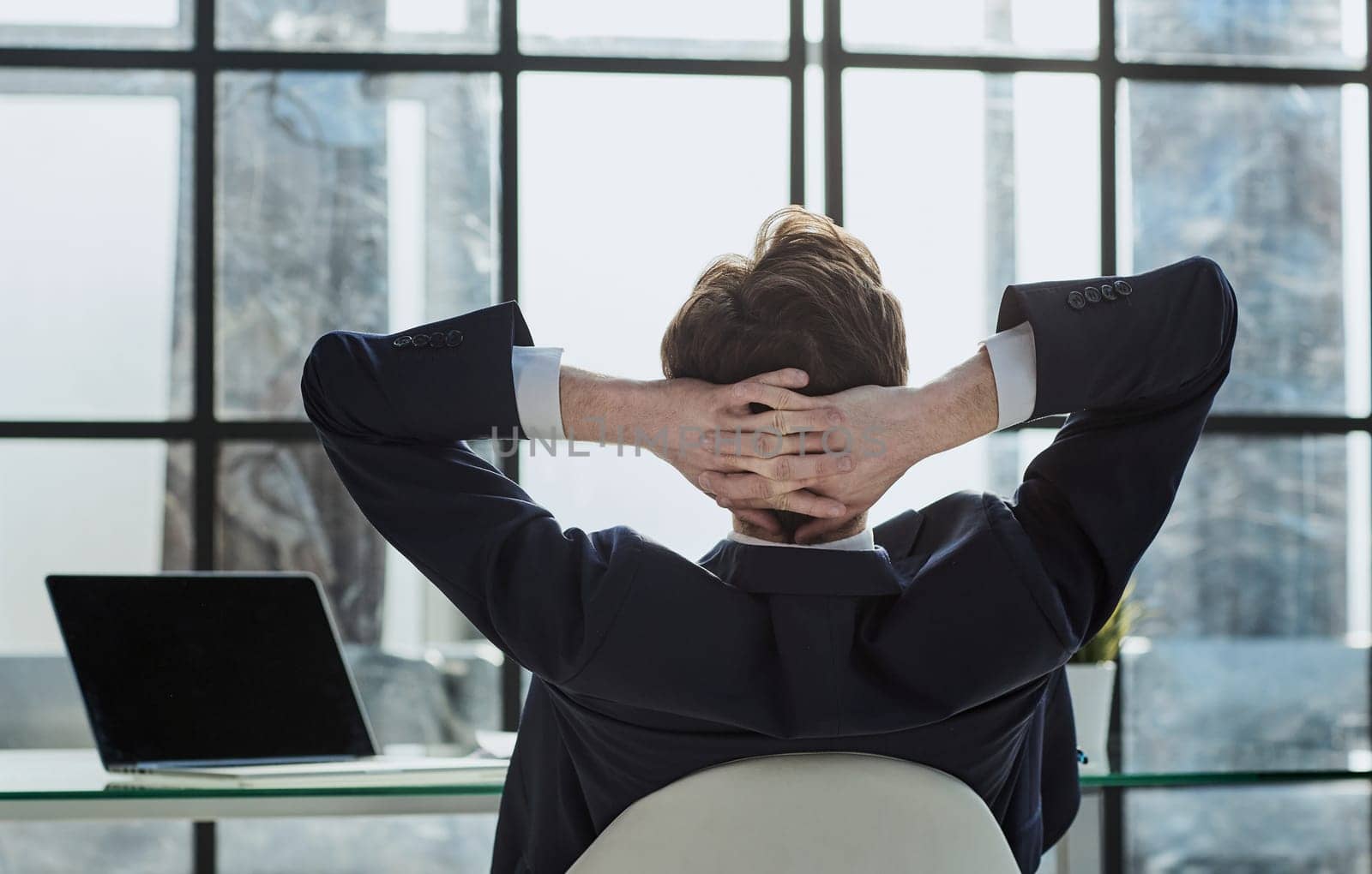 the worker sits in the office with his hands behind his head and looks out the window