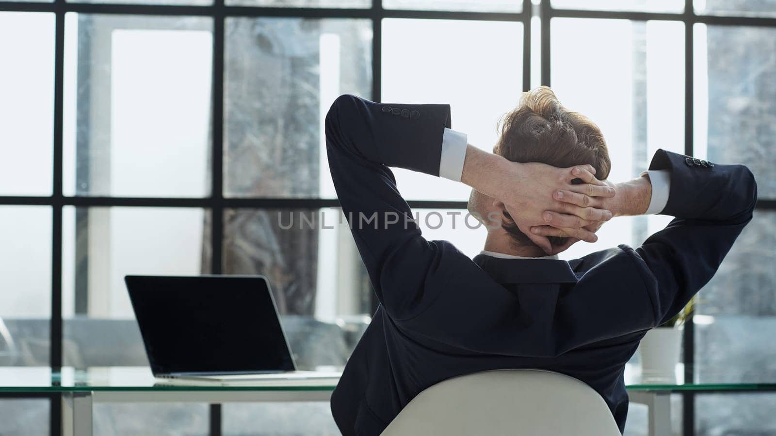 the worker sits in the office with his hands behind his head and looks out the window