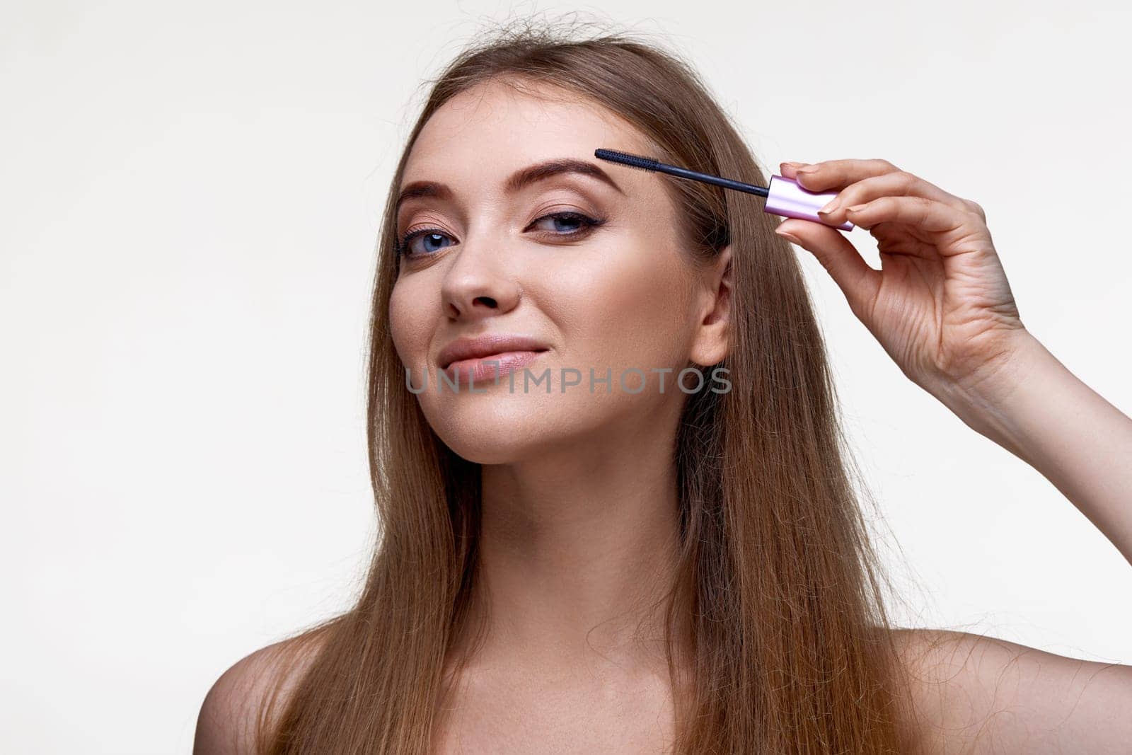 Beautiful young woman applying black mascara on long thick eyelashes with a brush and making night makeup on white background