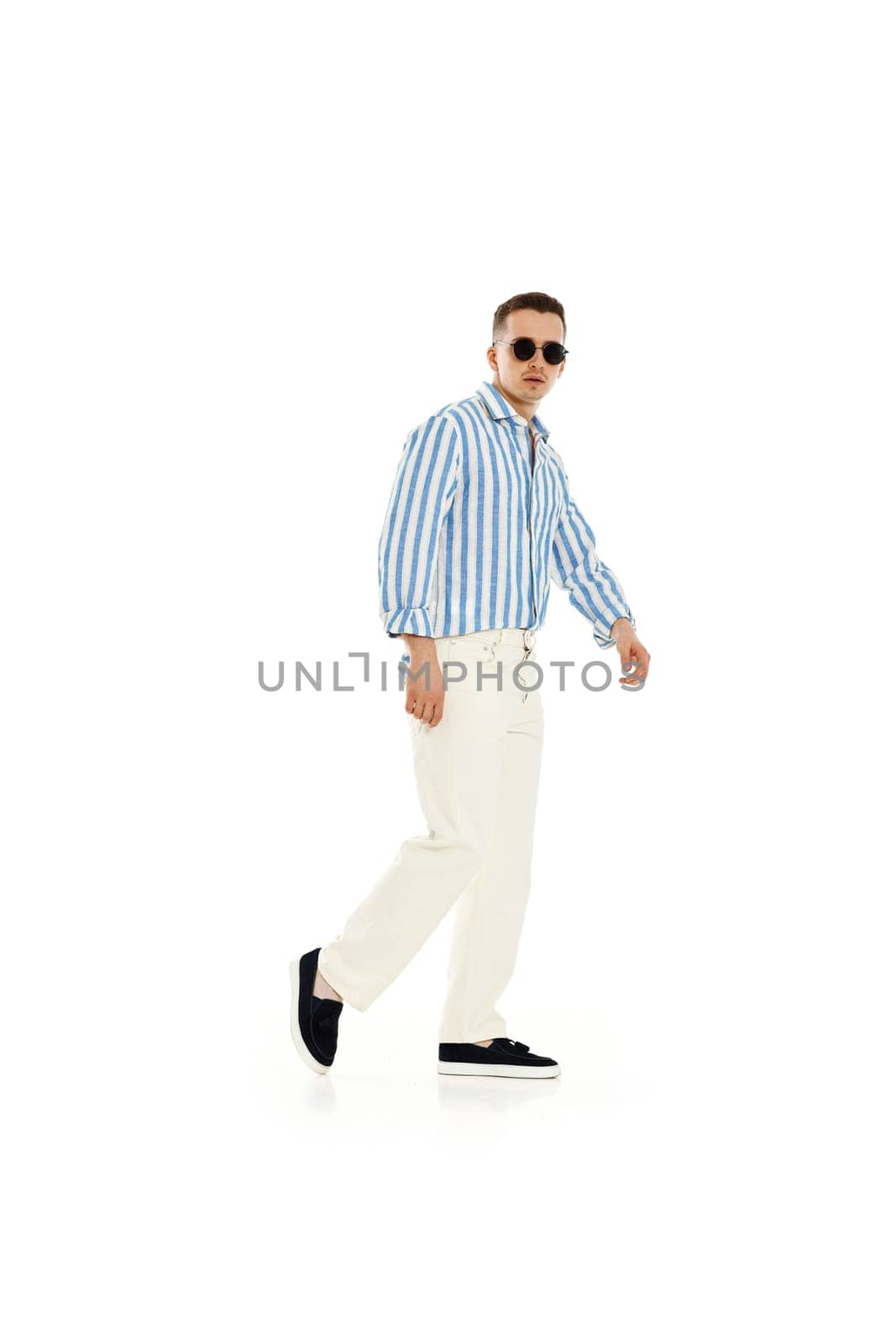 Young fashionable guy in trendy sunglasses, blue striped shirt and trousers isolated on white background. full length.