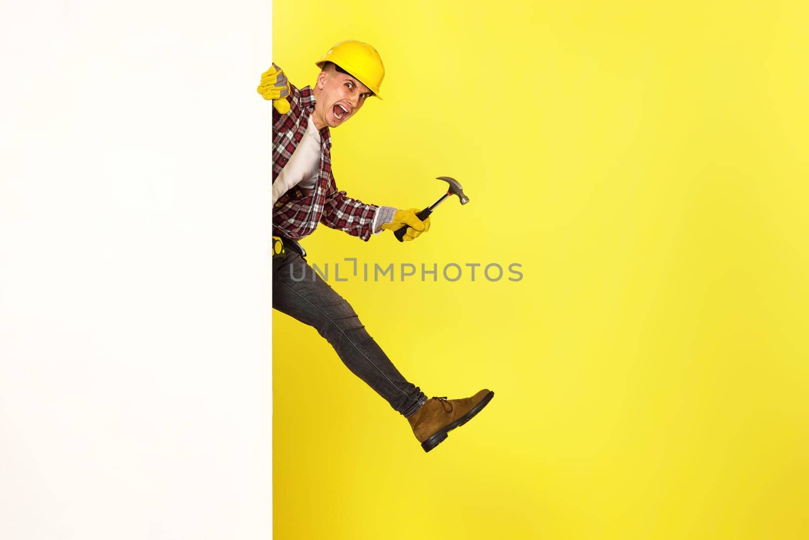 professional builder in work clothes, helmet holds hammer and comes out from behind the banner. copy space for text