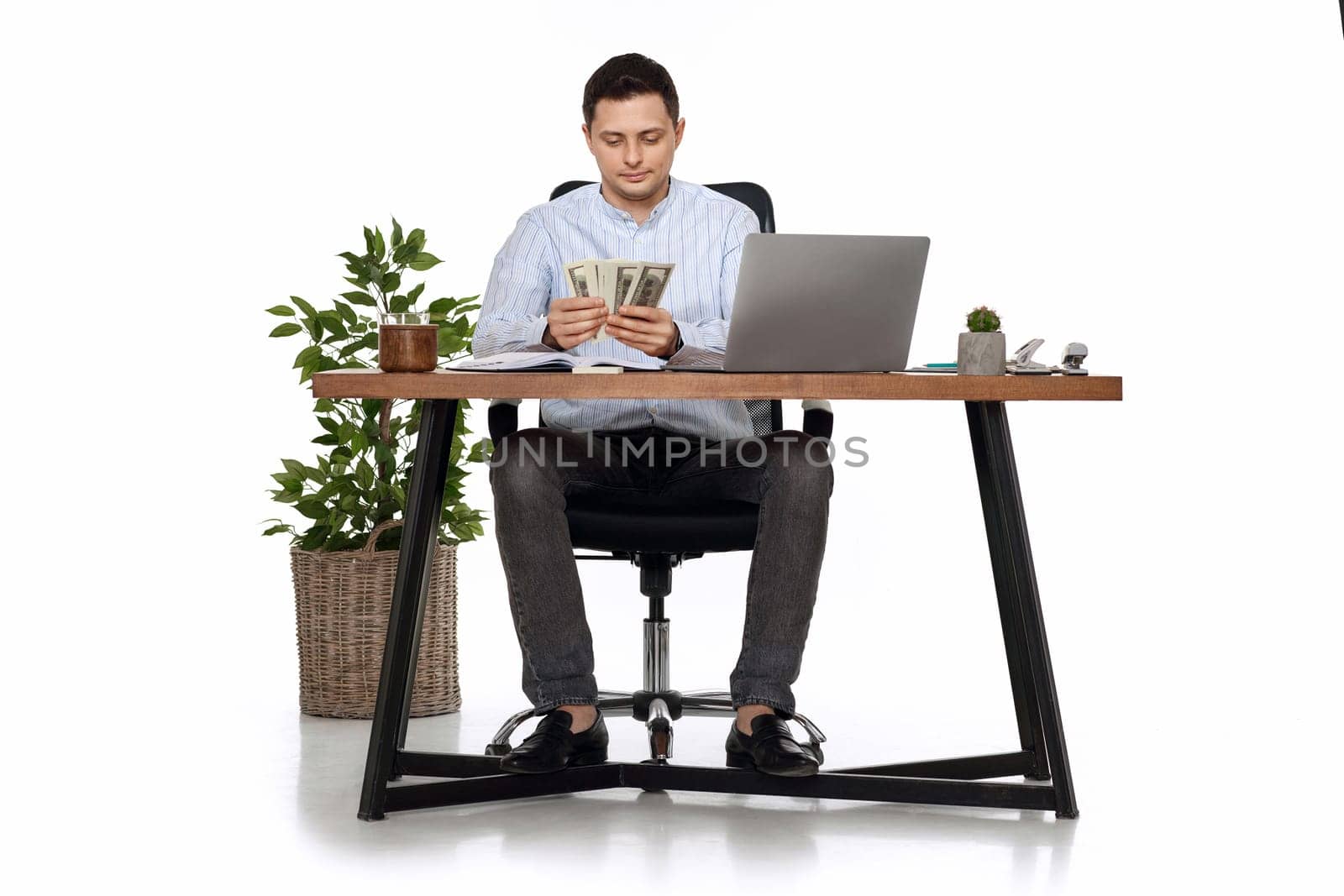 young handsome businessman working on laptop and holding money while sitting on chair at desk.