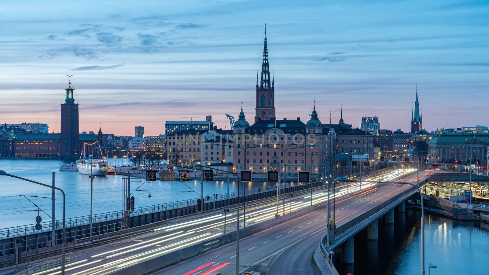 Photo of Light trails on a bridge to Stockholm at night. Silhouettes of old town against clear evening sky. Long exposure urban cityscape