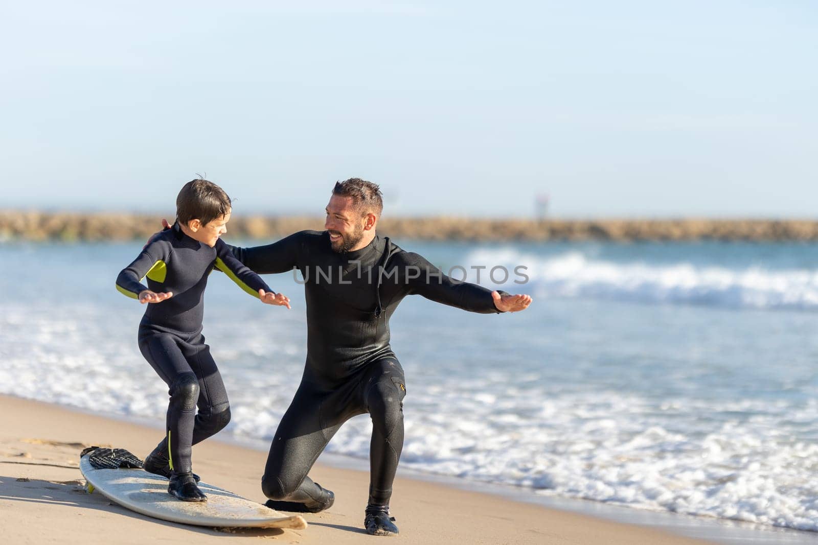 Smiling father teaching his son how to surf. Mid shot