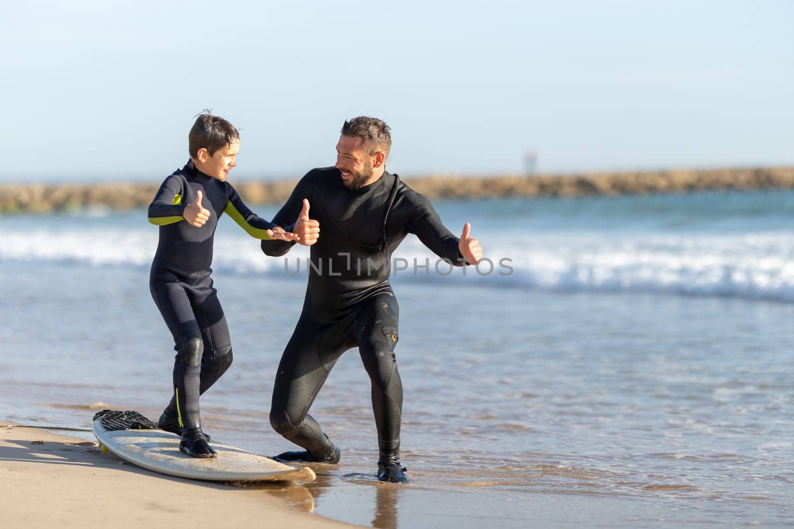 Smiling father teaching his son how to surf - showing a thumb up by Studia72