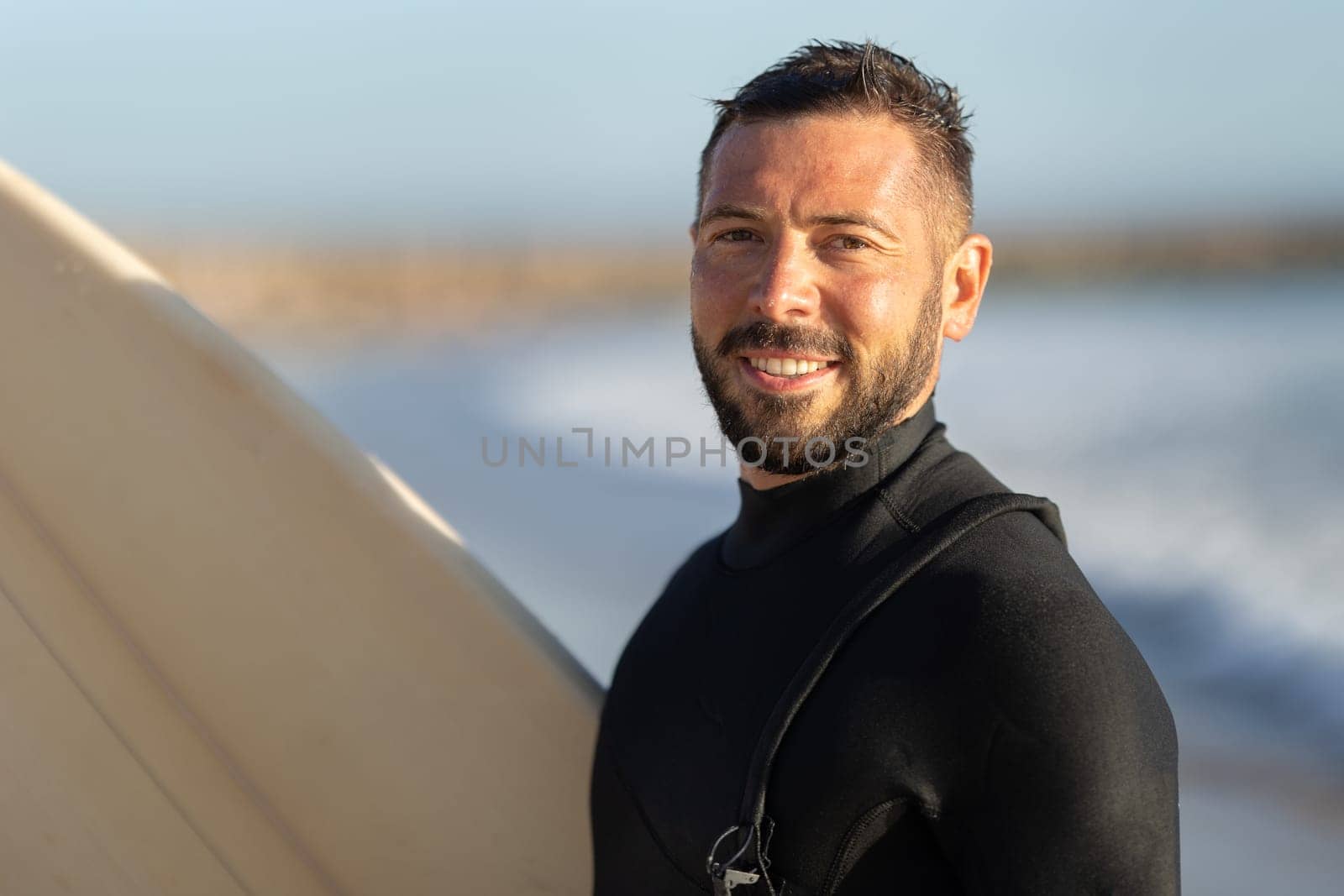 Smiling man surfer in a wetsuit looking in the camera. Portrait