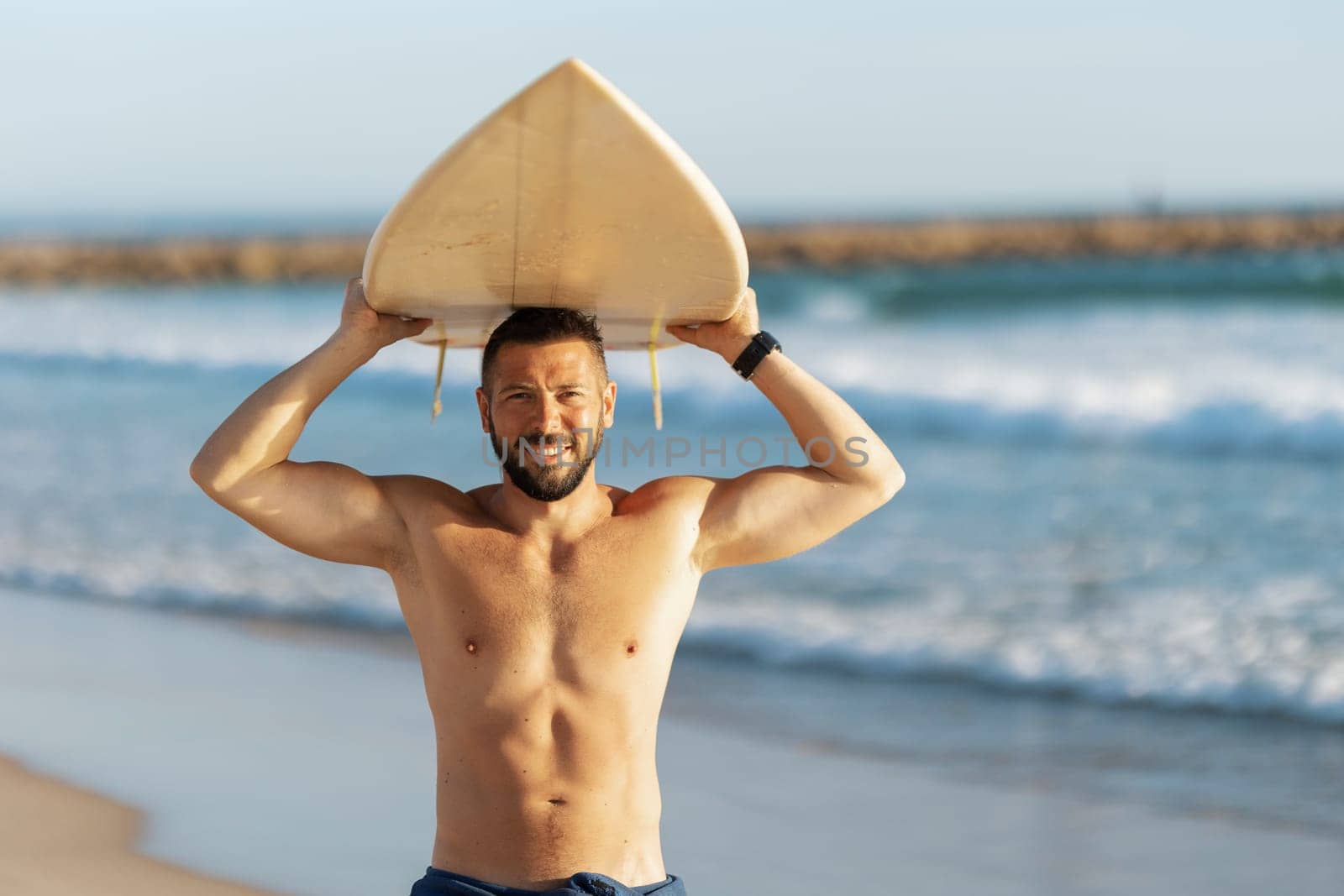 A man surfer with naked torso holding a surfing board over his head. Mid shot