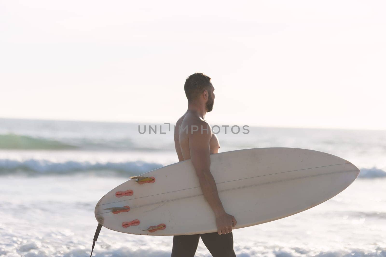 A man surfer with naked torso walking on the seashore. Mid shot
