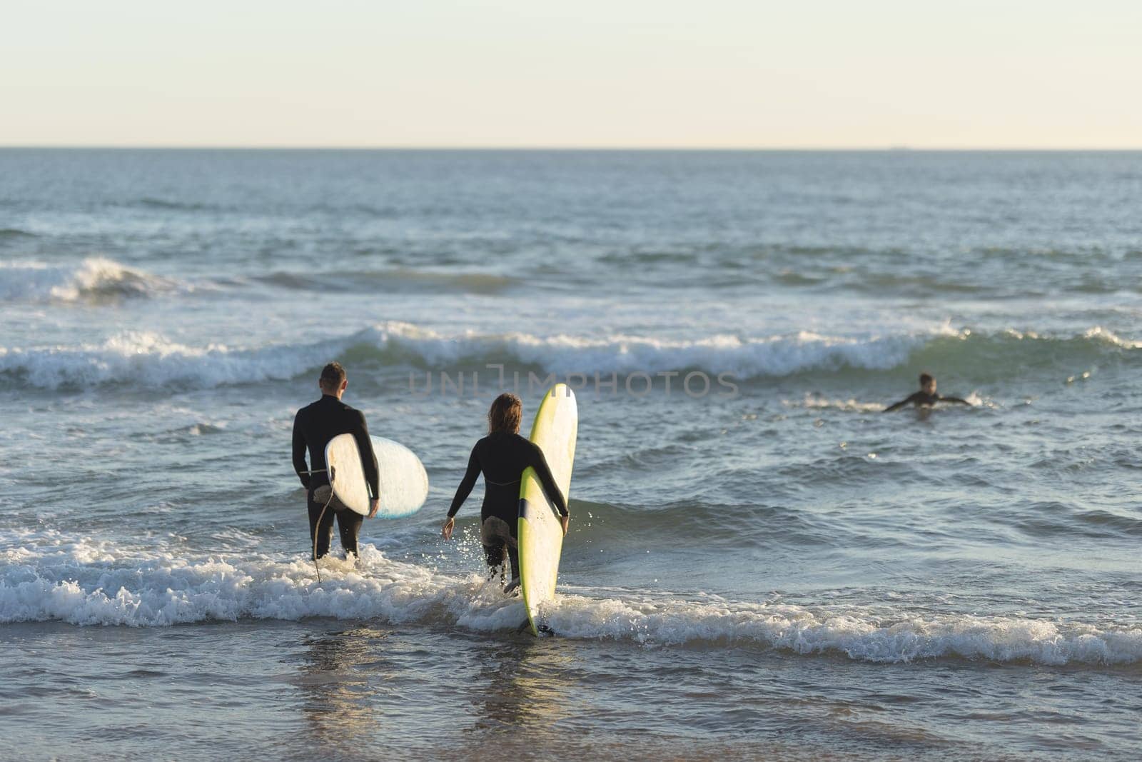 A man and a woman go out to sea holding surfboards. Mid shot