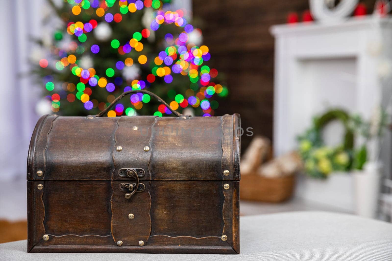 In front you can see an old brown box and against the fuzzy background stands a Christmas tree decorated with glowing Christmas tree lights.
