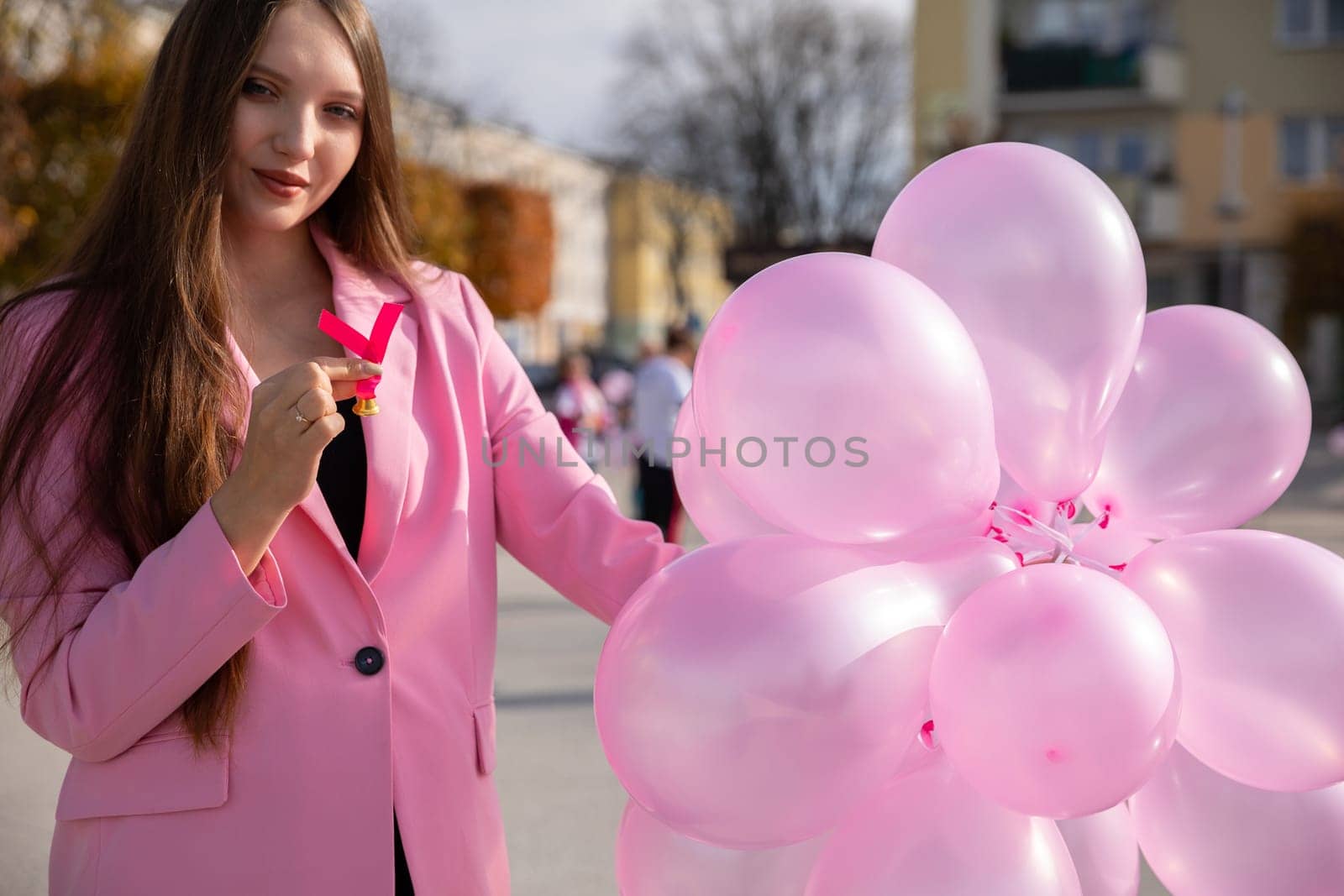 Woman in pink jacket promotes preventive breast examinations. Pink balloons and a ribbon to symbolize preventive research related to breast cancer.