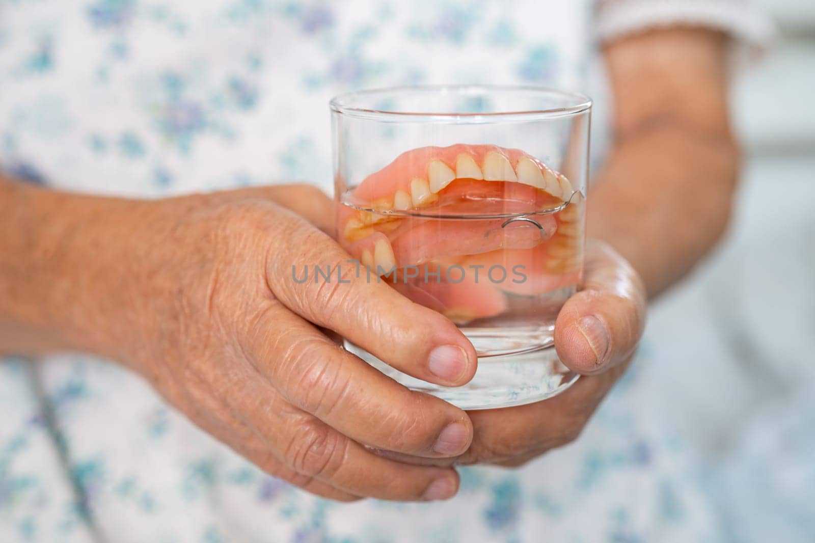 Asian senior woman patient holding and washing denture in water cleanser glass for good chewing.