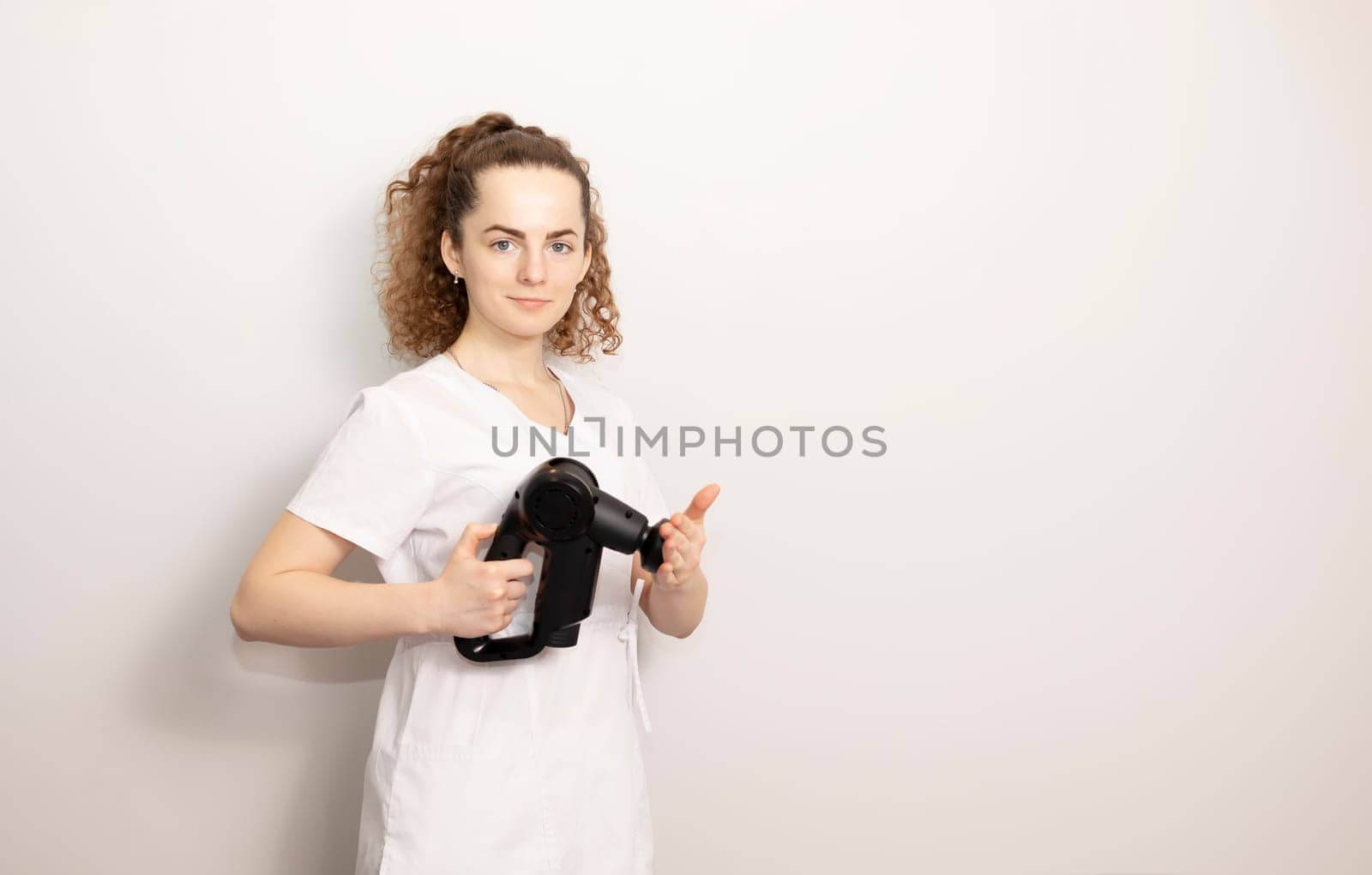 Rehabilitation Specialist, Physical Therapist In White Medical Clothes Holds Massage Gun, Massager Product, Copy Space For Text. Health Specialist, Rehabilitation. Horizontal plane by netatsi