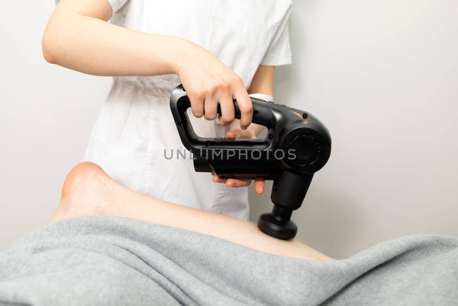 Rehabilitologist, Physical Therapist In White Medical Clothes Makes Leg Massage With Massager Product, Gun. Health Specialist, Rehabilitation, Healthcare. Horizontal plane.