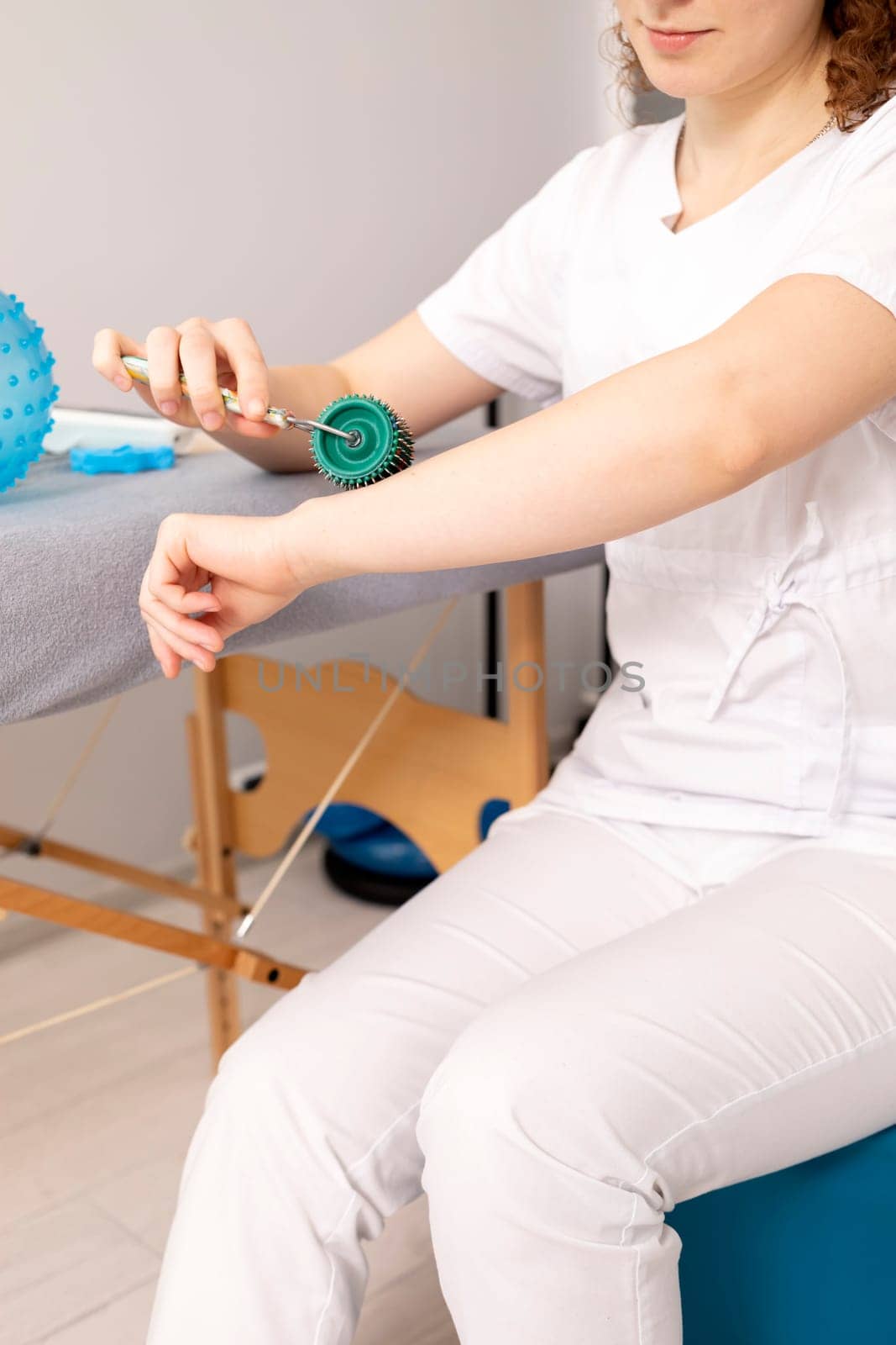 Rehabilitation Specialist, Physical Therapist Demonstrates Rehab Tool Meso Roller With Titanium Needles On Hand, Massage Ball With Pimples in Therapeutic Room. Healthcare, Rehabilitation. Vertical.